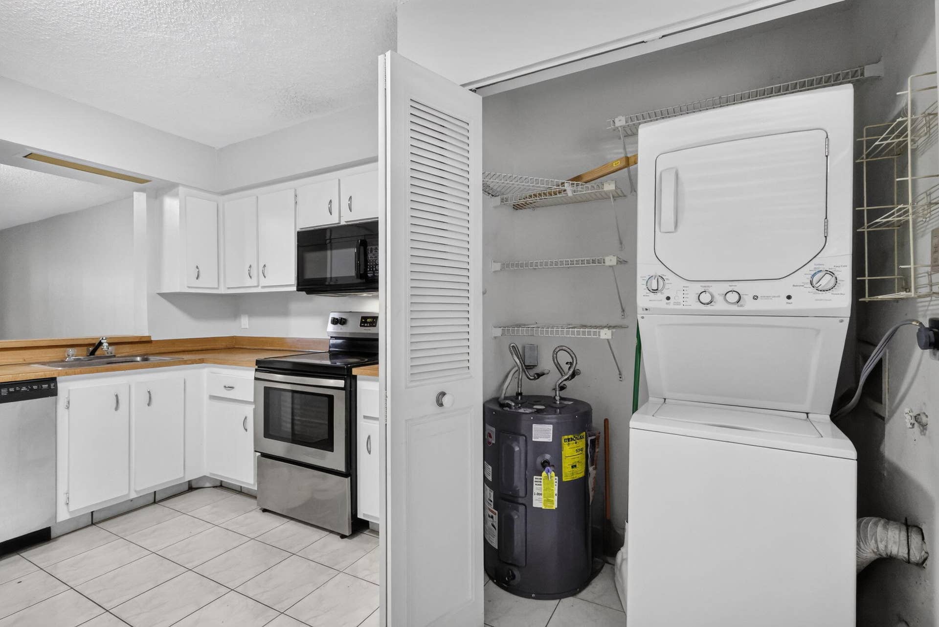 14527 BONAIRE Boulevard, #109, Delray Beach, FL 33446 Kitchen featuring white cabinetry, stainless steel appliances, tile flooring, and an integrated laundry closet with a stacked washer and dryer unit