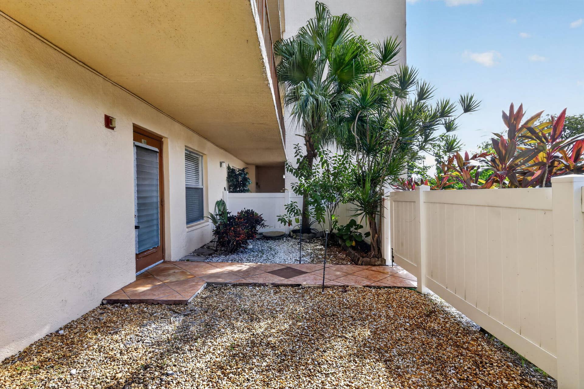 14527 BONAIRE Boulevard, #109, Delray Beach, FL 33446 Private patio featuring tile flooring, stone landscaping, and a white privacy fence