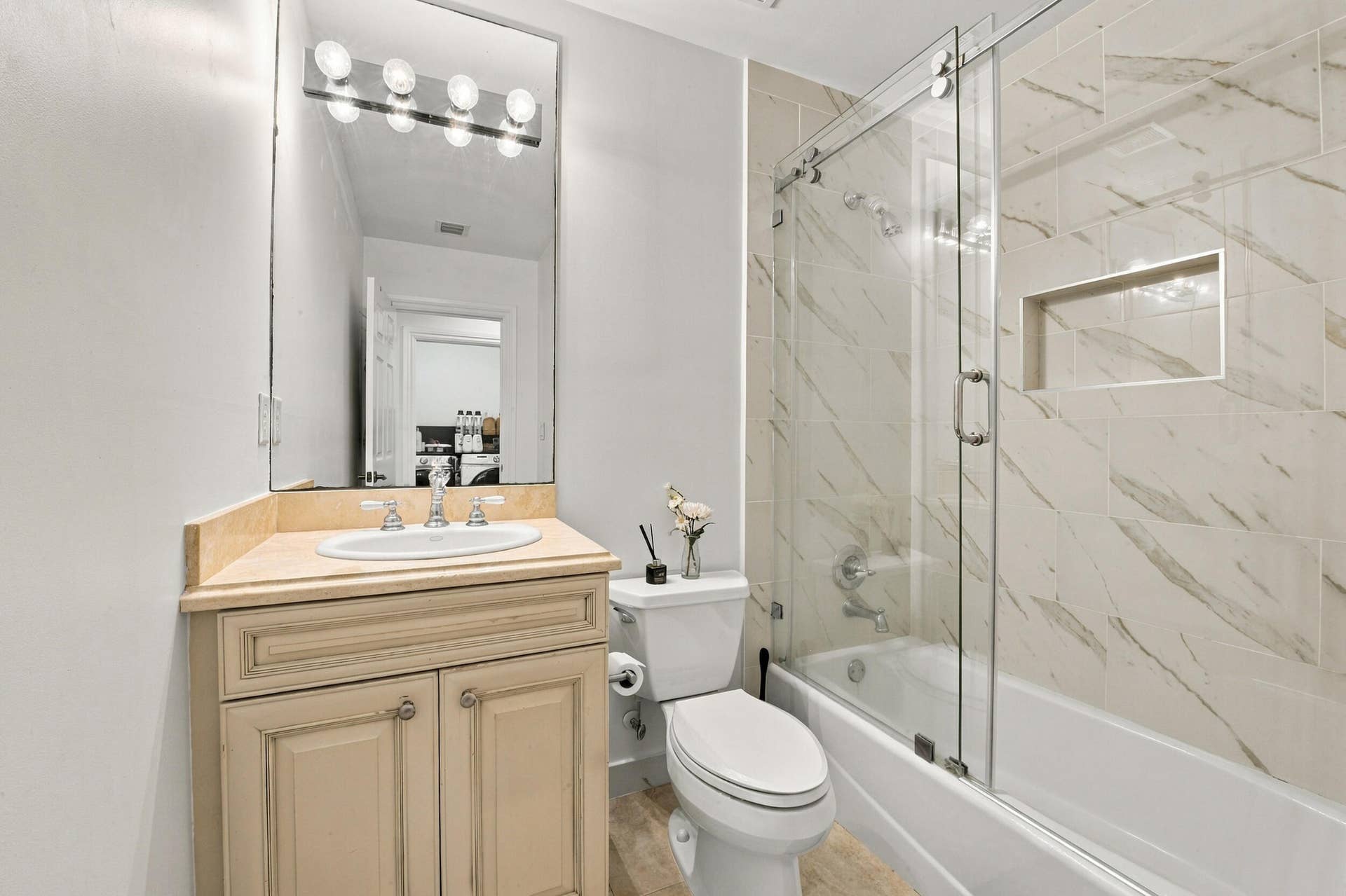 1752 NE 12TH Street, Fort Lauderdale, FL 33304 Bathroom featuring a vanity with a light-finish cabinet and an integrated oval sink, a frameless sliding glass shower door, and a shower enclosure tiled with a stone-finish surround featuring an integrated storage niche