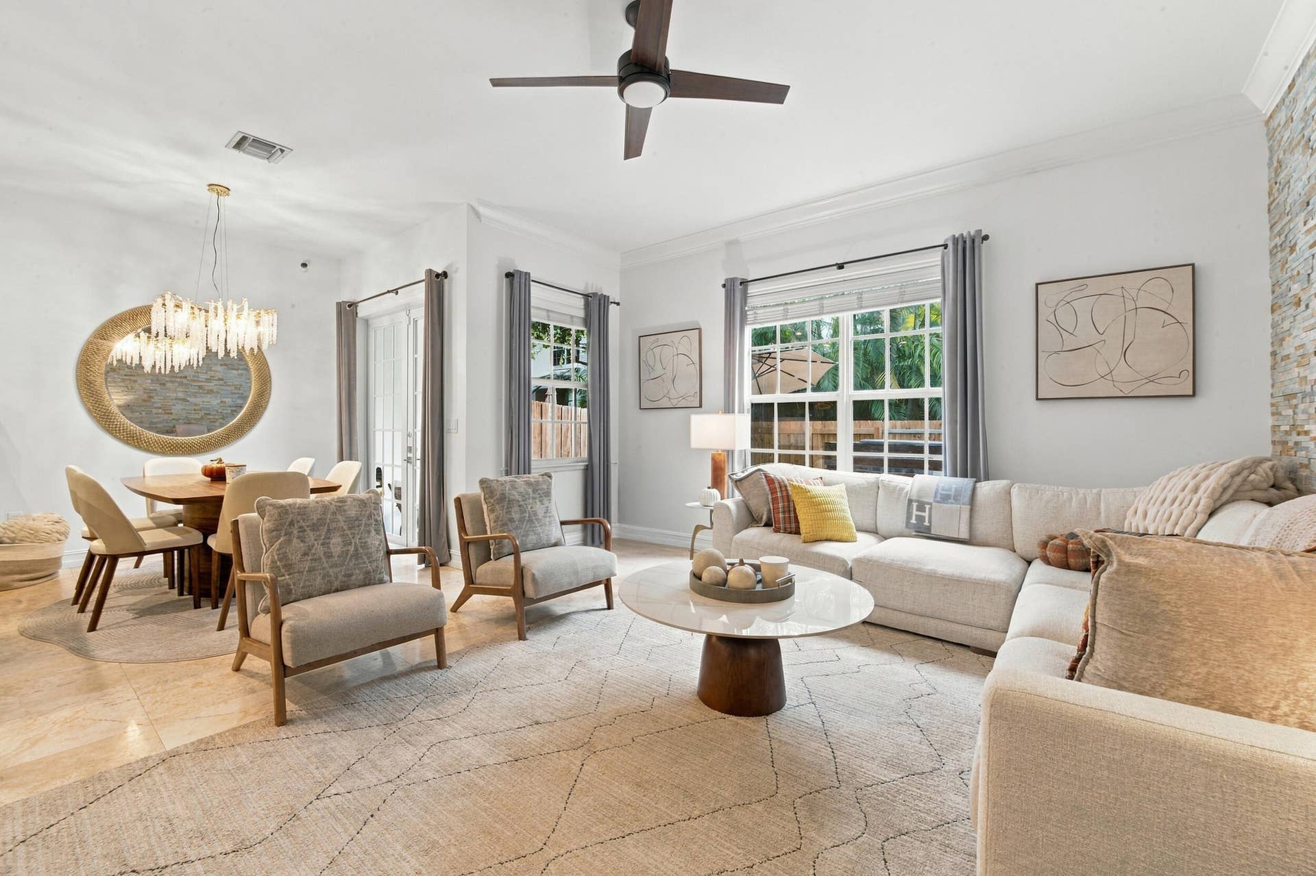 1752 NE 12TH Street, Fort Lauderdale, FL 33304 Open living area featuring large-format tile flooring, a stone-accented wall, crown molding, multi-light chandelier, and ceiling fan