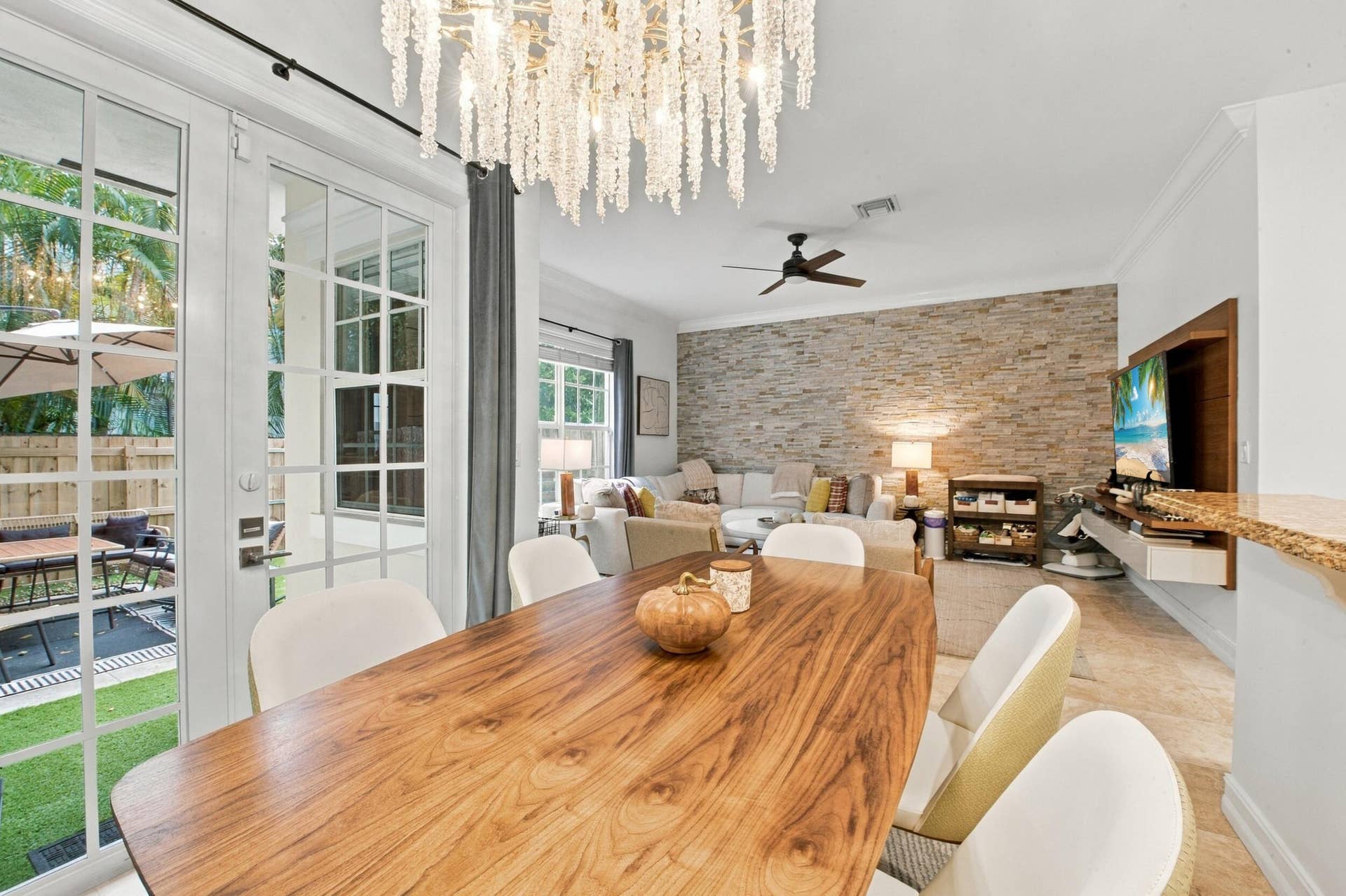 1752 NE 12TH Street, Fort Lauderdale, FL 33304 Interior space featuring a stacked stone accent wall, decorative tiered chandelier, French doors with glass panes, crown molding, and neutral tile flooring