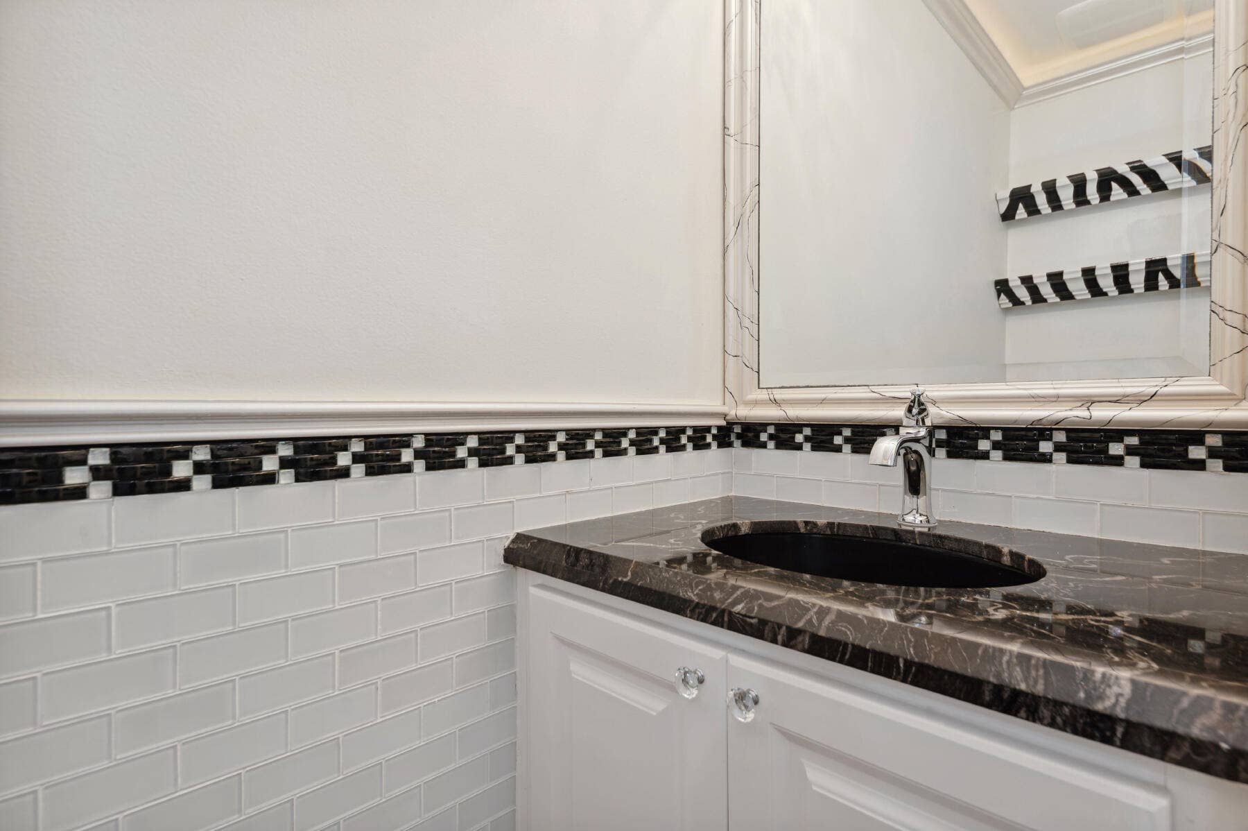477 Capistrano Drive, Palm Beach Gardens, Palm Beach Gardens, FL 33410 Vanity featuring a dark stone countertop, undermount oval sink, polished chrome faucet, white cabinetry with crystal-style hardware, and a subway tile backsplash with a decorative checkered border