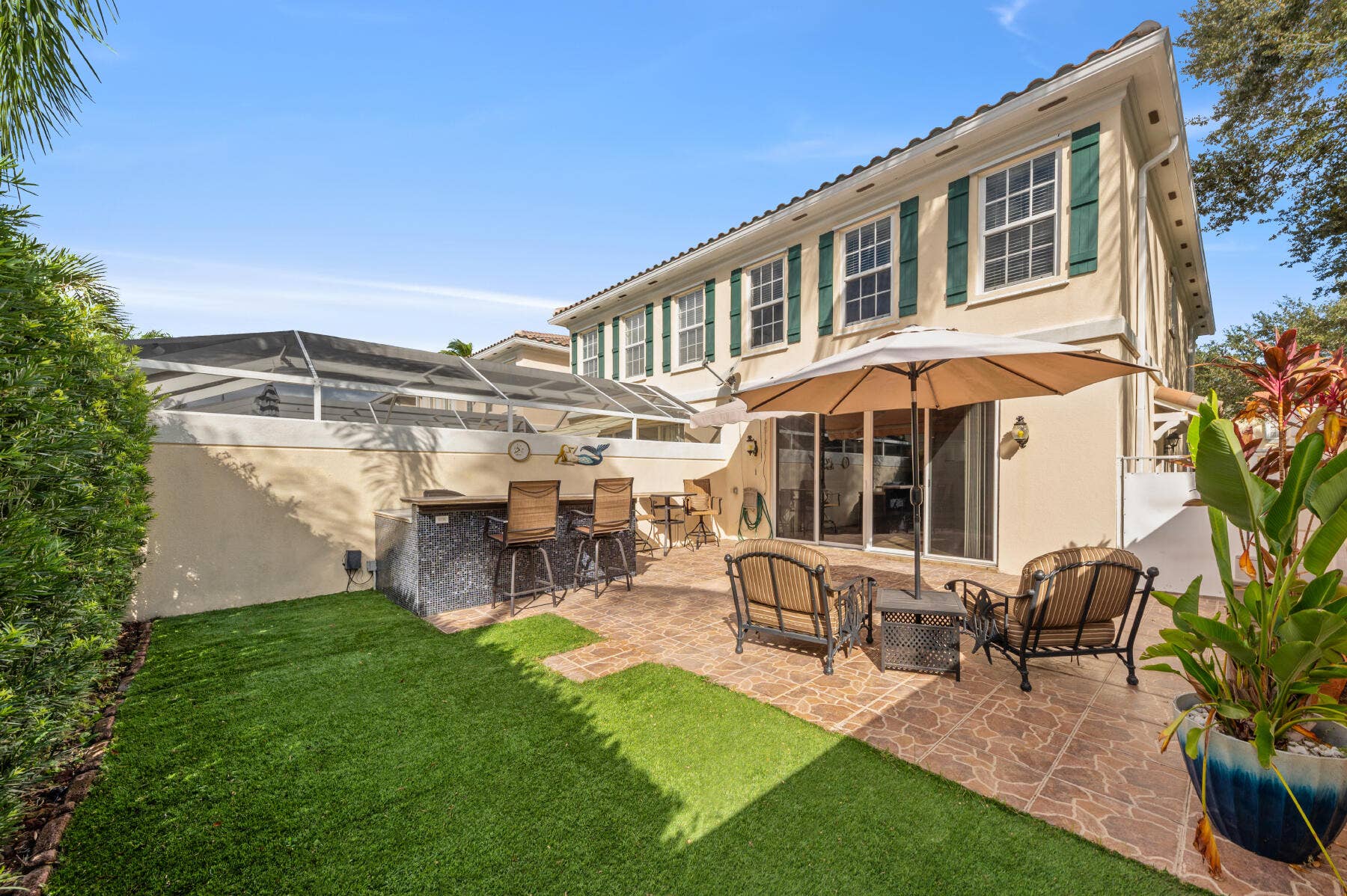 477 Capistrano Drive, Palm Beach Gardens, Palm Beach Gardens, FL 33410 Exterior patio featuring a stone-tile floor, outdoor bar with a stone-finish counter, synthetic turf area, and screened-in enclosure