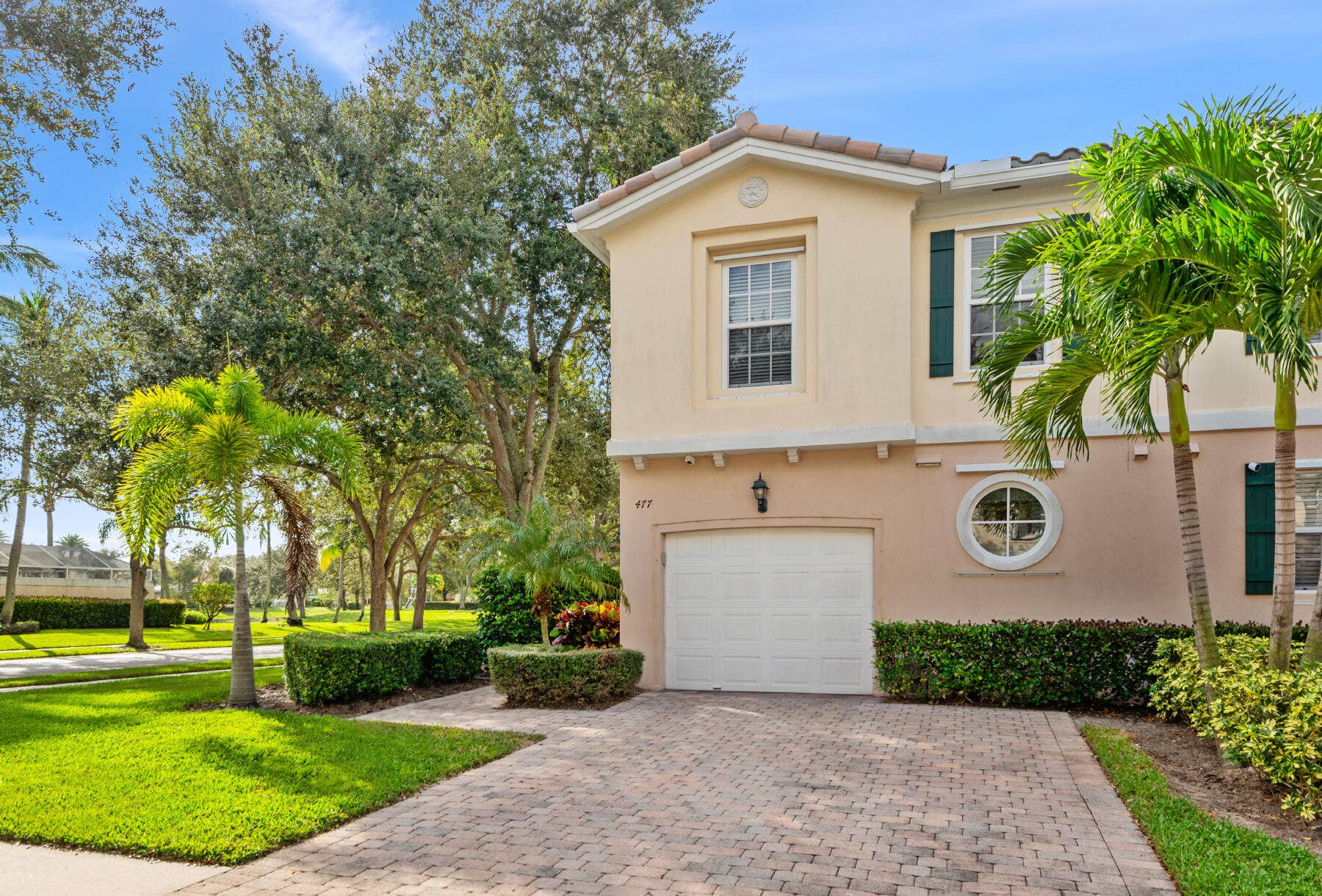 477 Capistrano Drive, Palm Beach Gardens, Palm Beach Gardens, FL 33410 Two-story residence featuring a paved stone driveway, single-car garage, stucco exterior, accent shutters, and circular window detailing