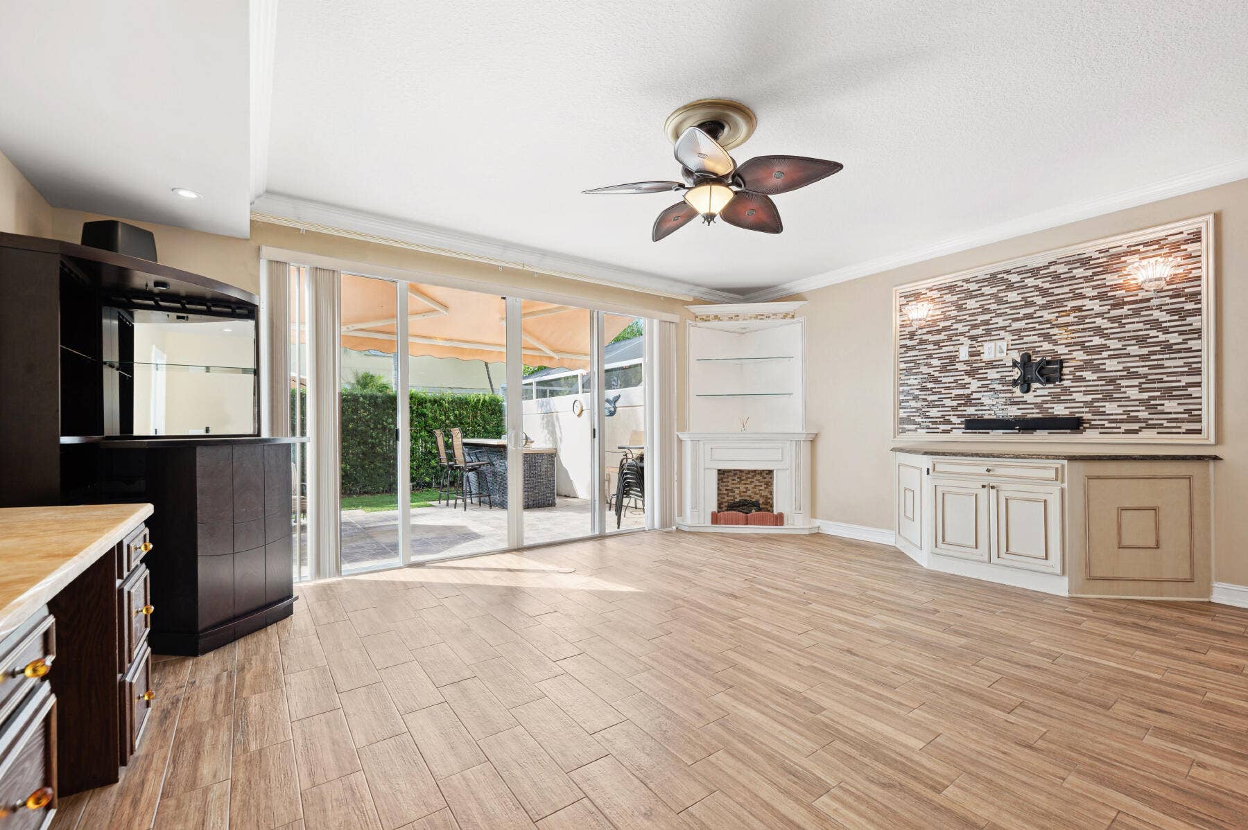 477 Capistrano Drive, Palm Beach Gardens, Palm Beach Gardens, FL 33410 Living space featuring wood-finish flooring, a corner fireplace with built-in shelving, a stone-tiled media wall, multi-panel glass sliding doors, and a ceiling fan with integrated lighting