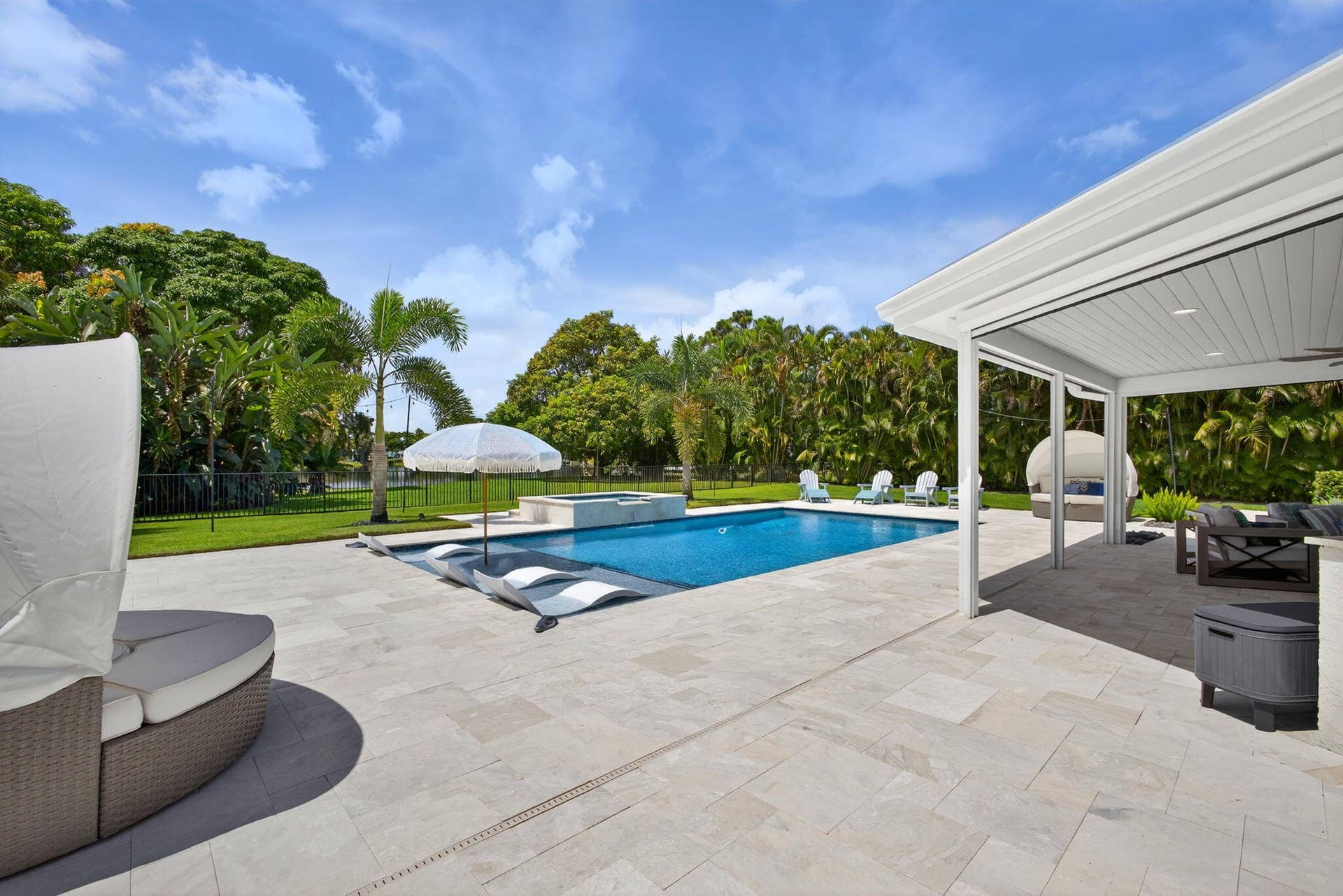4628 Square Lake Drive, Palm Beach Gardens, FL 33418 Outdoor living area featuring a covered lanai with a beadboard ceiling, expansive stone paver patio, swimming pool with an integrated spa, and manicured lawn