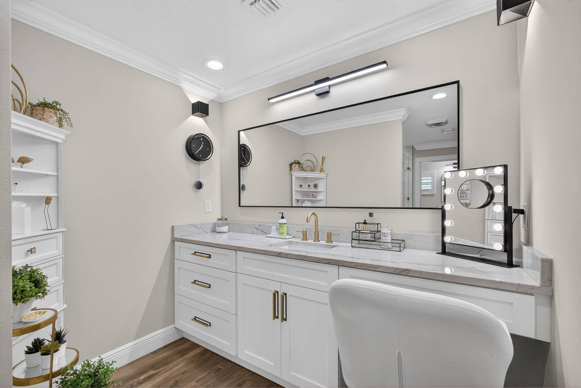 4628 Square Lake Drive, Palm Beach Gardens, FL 33418 White vanity cabinetry featuring gold-tone hardware, stone-finish countertop with an integrated sink, polished gold-tone faucet, large rectangular mirror with a black frame, and linear LED vanity lighting