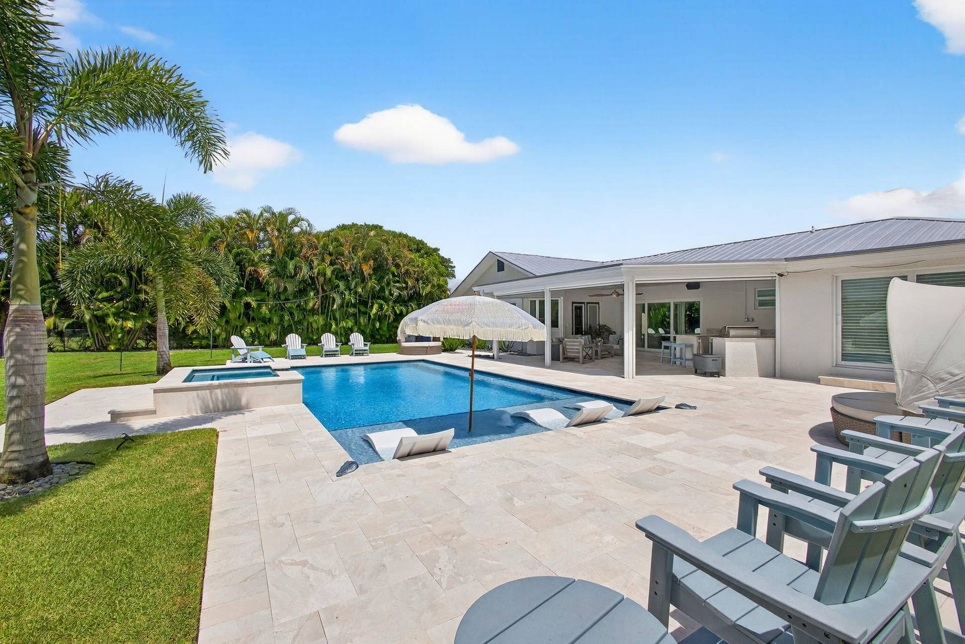 4628 Square Lake Drive, Palm Beach Gardens, FL 33418 Backyard oasis featuring an in-ground pool with a spillover spa, expansive light-toned stone patio, covered lanai, and manicured lawn