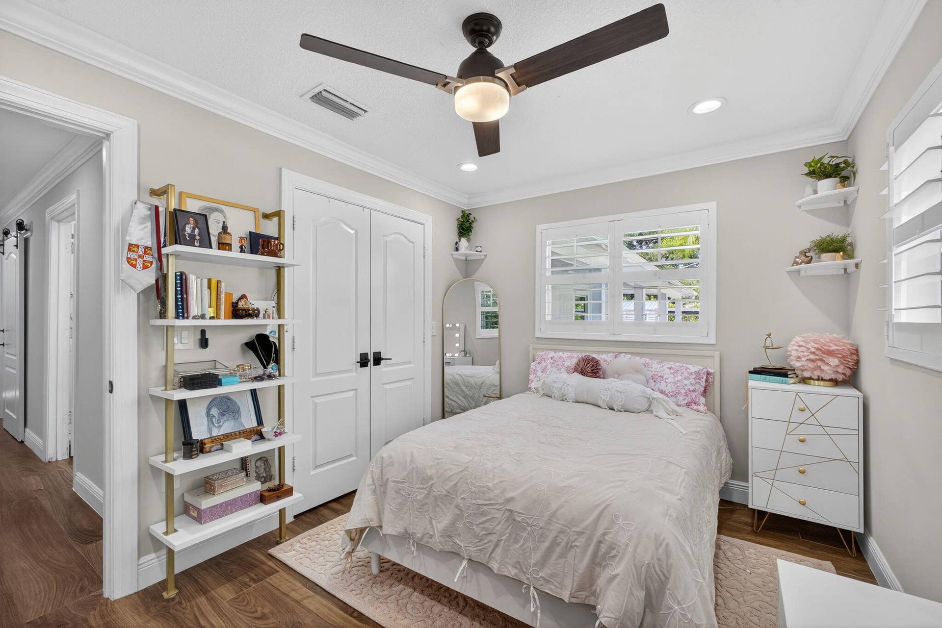 4628 Square Lake Drive, Palm Beach Gardens, FL 33418 Neutral interior featuring wood-finish flooring, crown molding, double-door closet with matte black hardware, dual-blade ceiling fan with integrated lighting, and white louvered plantation shutters