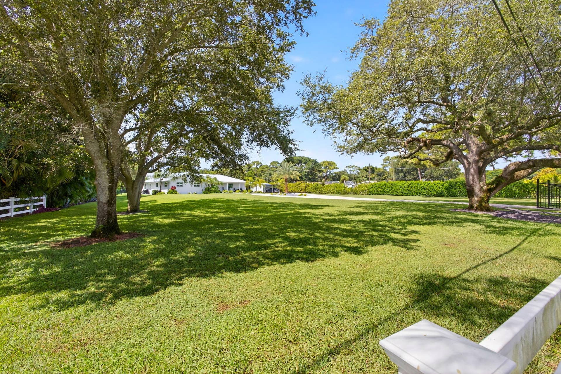 4628 Square Lake Drive, Palm Beach Gardens, FL 33418 Expansive yard featuring mature trees, white post-and-rail fencing, and manicured landscaping