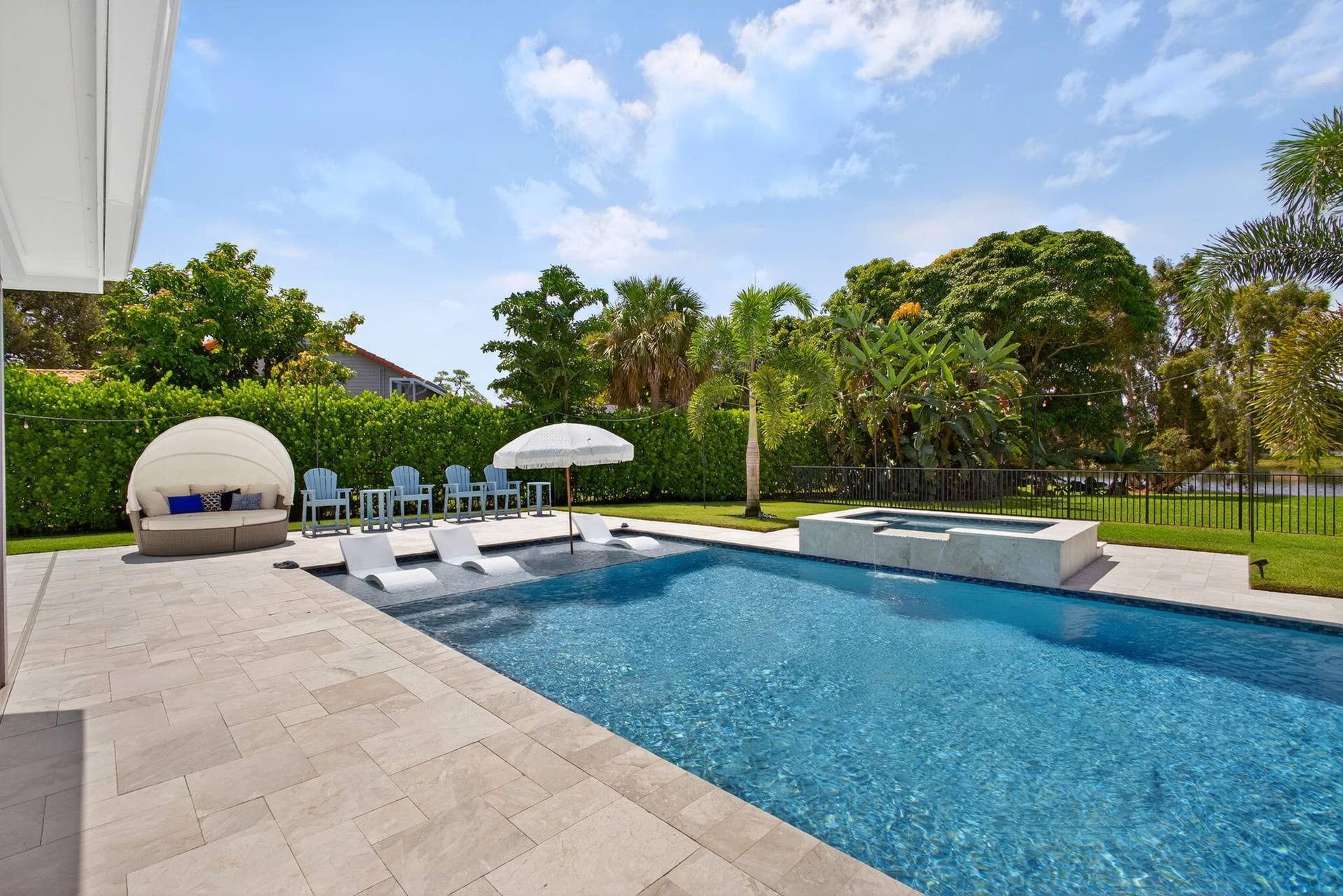 4628 Square Lake Drive, Palm Beach Gardens, FL 33418 Outdoor space featuring an in-ground pool with a tanning ledge, a raised integrated spa, stone-paver decking, and manicured privacy hedging