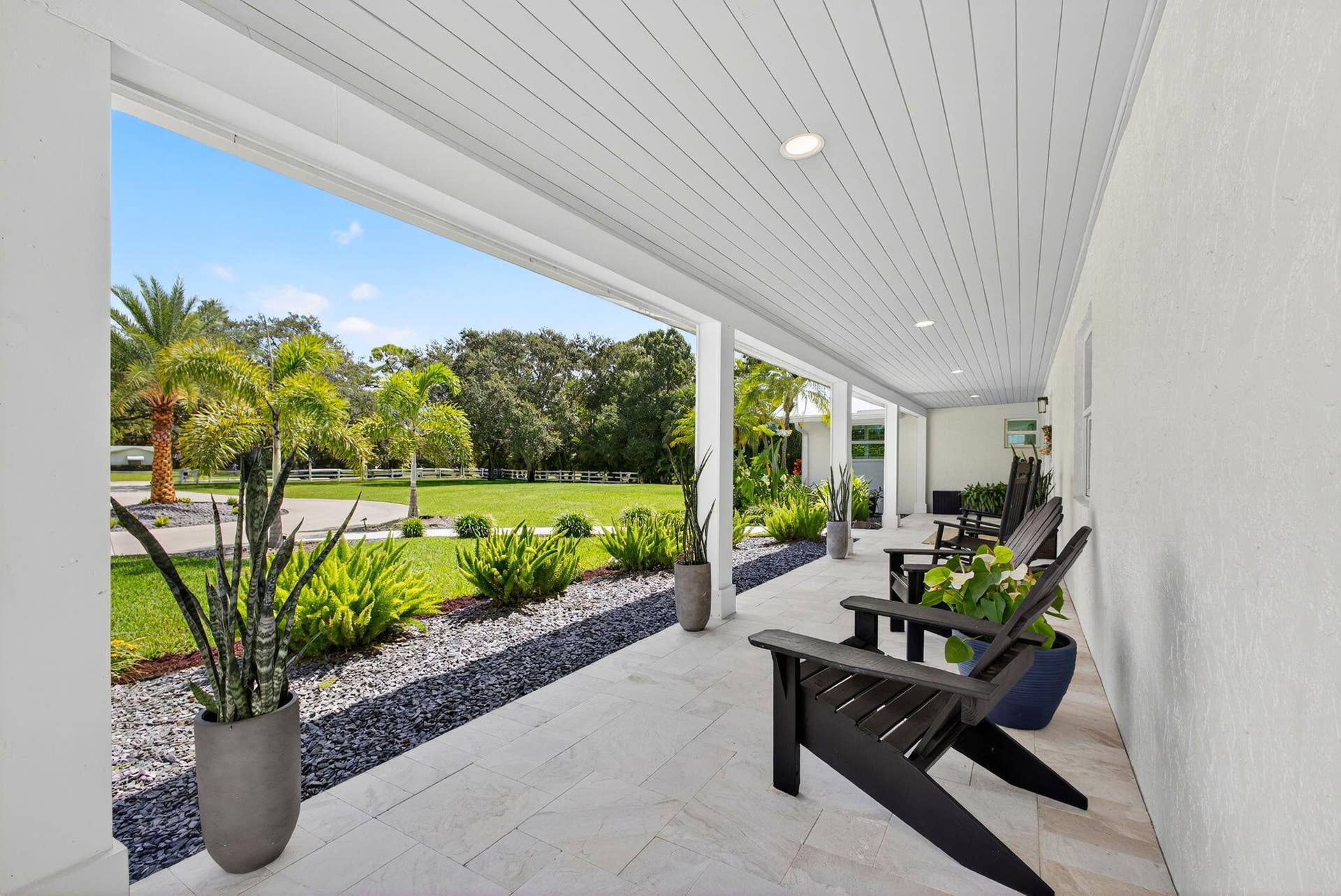 4628 Square Lake Drive, Palm Beach Gardens, FL 33418 Covered porch featuring stone-finish flooring, recessed lighting, and a beadboard ceiling, overlooking a landscaped lawn with crushed stone borders