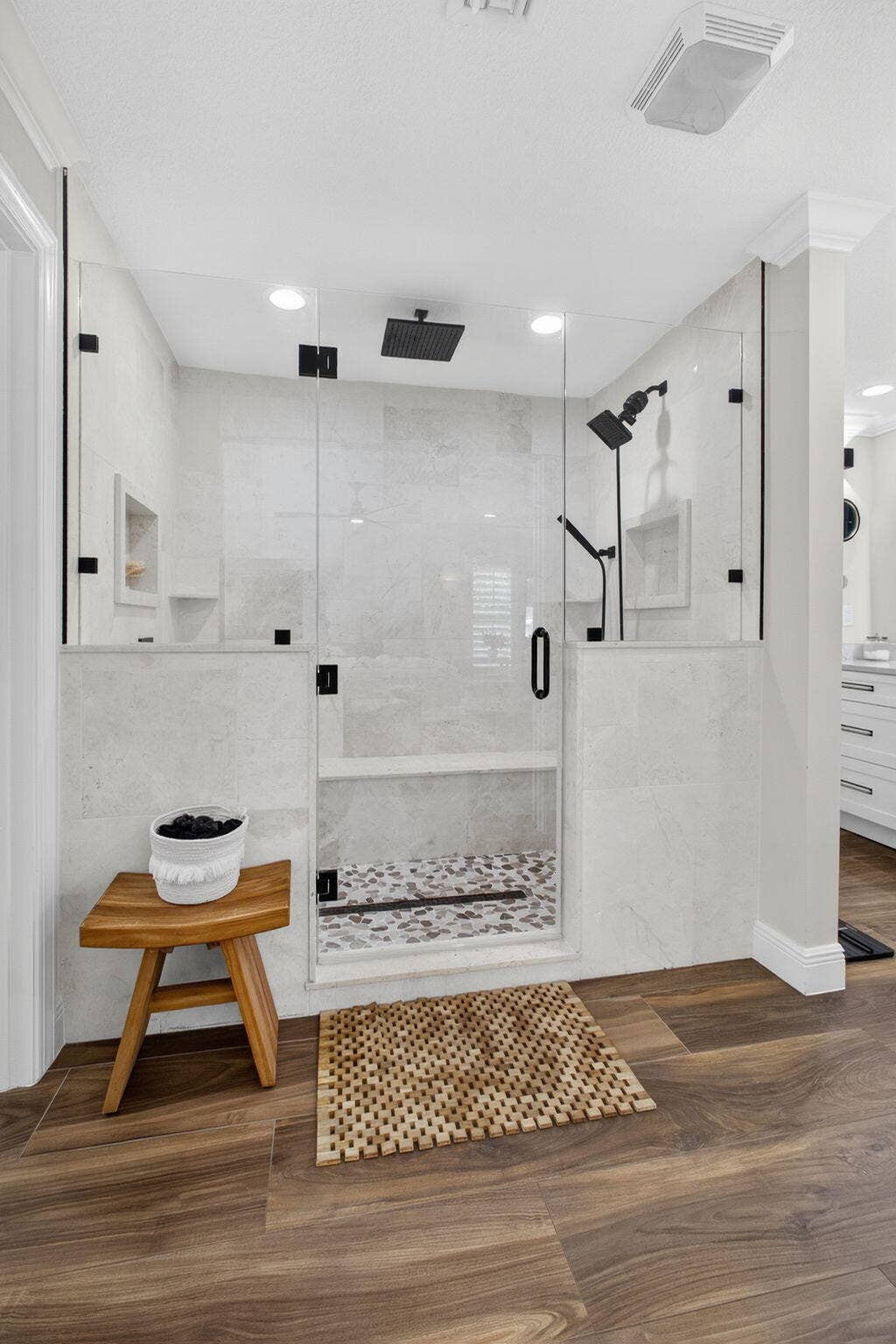 4628 Square Lake Drive, Palm Beach Gardens, FL 33418 Walk-in shower featuring a frameless glass enclosure, matte black fixtures, integrated shelving, and multi-tone mosaic tile flooring, accented by wood-finish flooring