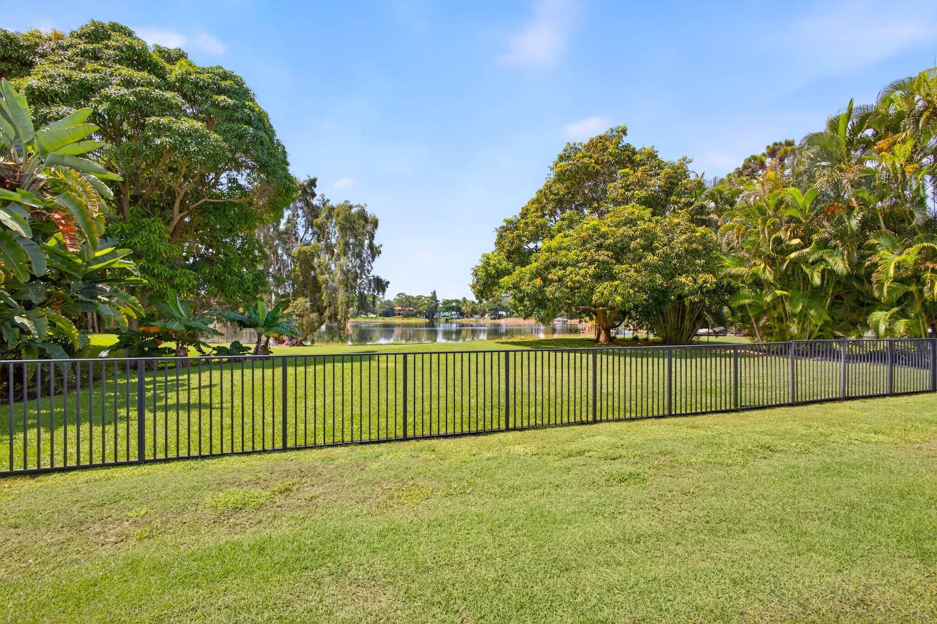 4628 Square Lake Drive, Palm Beach Gardens, FL 33418 Expansive lawn featuring a black metal perimeter fence and mature trees