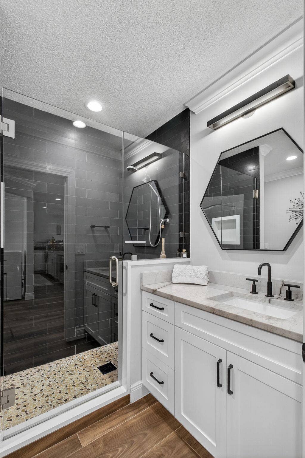 4628 Square Lake Drive, Palm Beach Gardens, FL 33418 White shaker-style vanity with stone countertop, undermount sink, and matte black hardware, paired with a glass-enclosed shower featuring stone flooring, subway tile walls, and a recessed niche