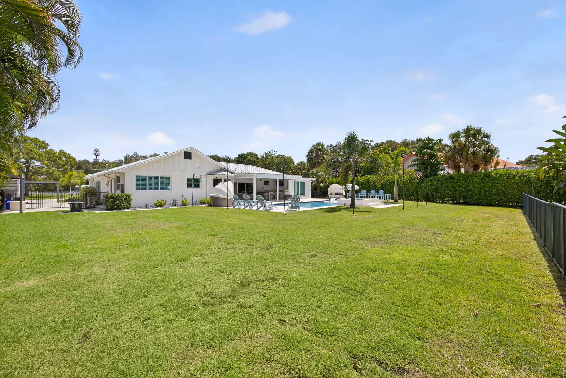 4628 Square Lake Drive, Palm Beach Gardens, FL 33418 Expansive backyard featuring a large grass lawn, swimming pool, covered patio area, and mature perimeter landscaping