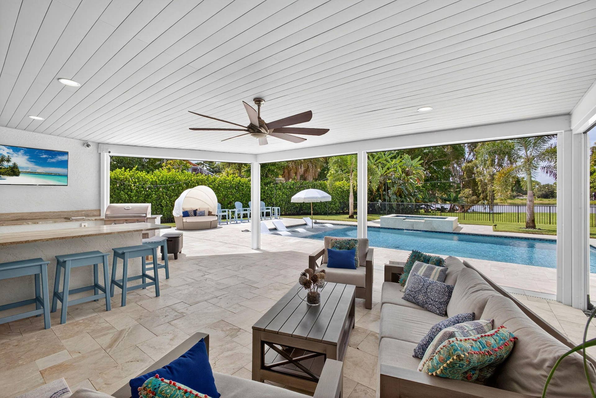 4628 Square Lake Drive, Palm Beach Gardens, FL 33418 Covered outdoor living space featuring a stone-tile patio, built-in kitchen with stone-top bar, recessed lighting, ceiling fan, and swimming pool with a raised spillover spa