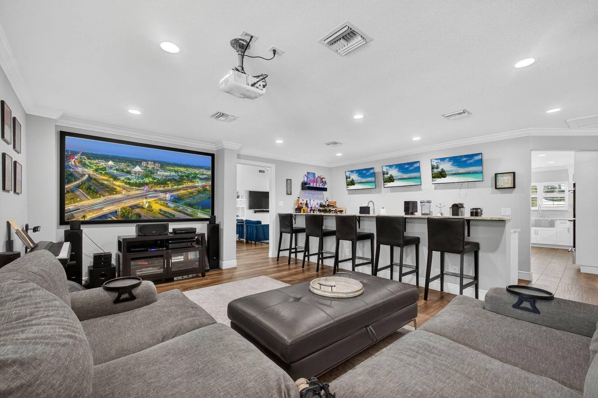4628 Square Lake Drive, Palm Beach Gardens, FL 33418 Custom entertainment space featuring a large-format projector screen, recessed ceiling lighting, wood-finish flooring, and a built-in wet bar with a countertop