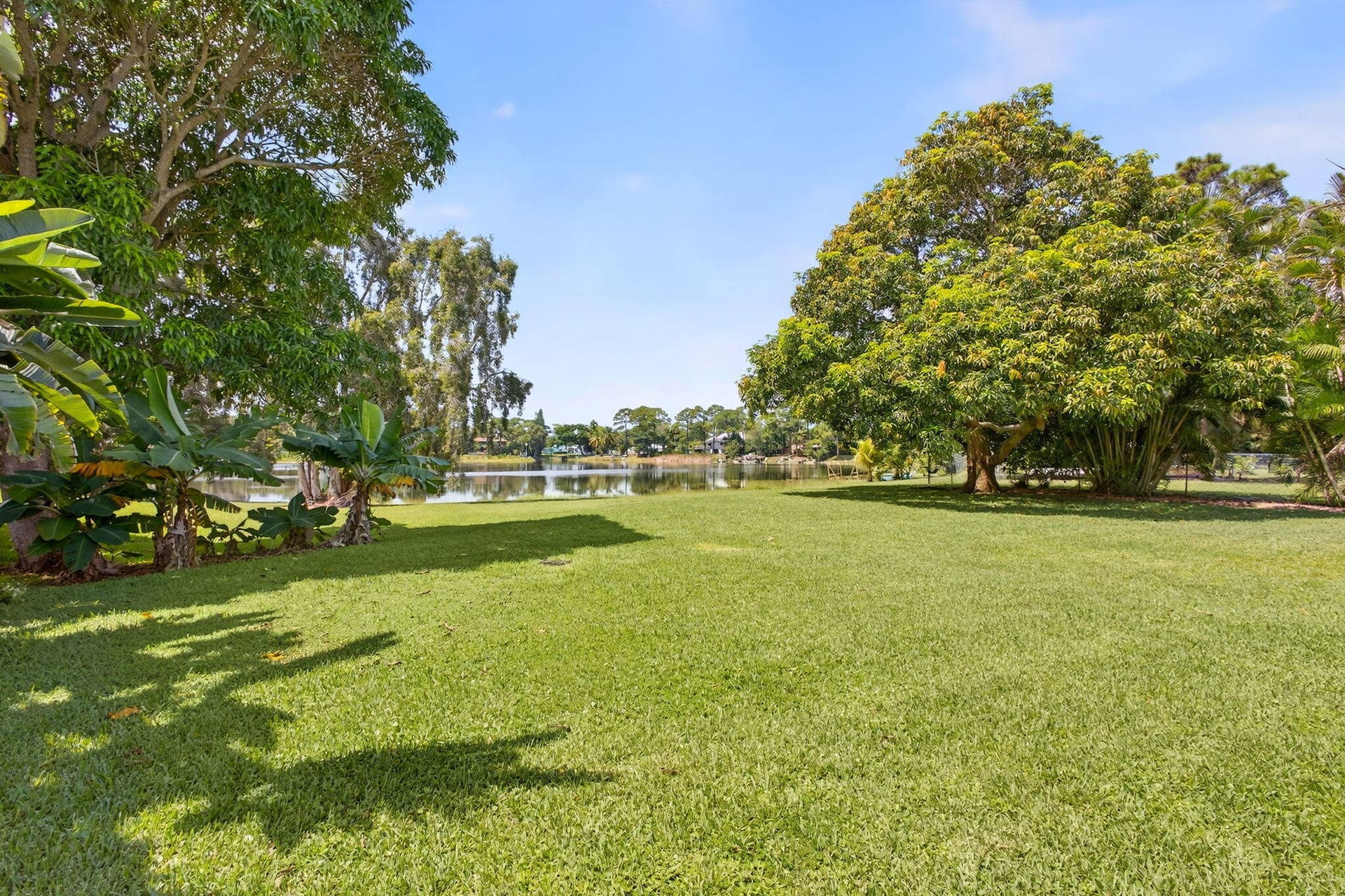 4628 Square Lake Drive, Palm Beach Gardens, FL 33418 Expansive grassy backyard featuring mature shade trees and direct waterfront frontage