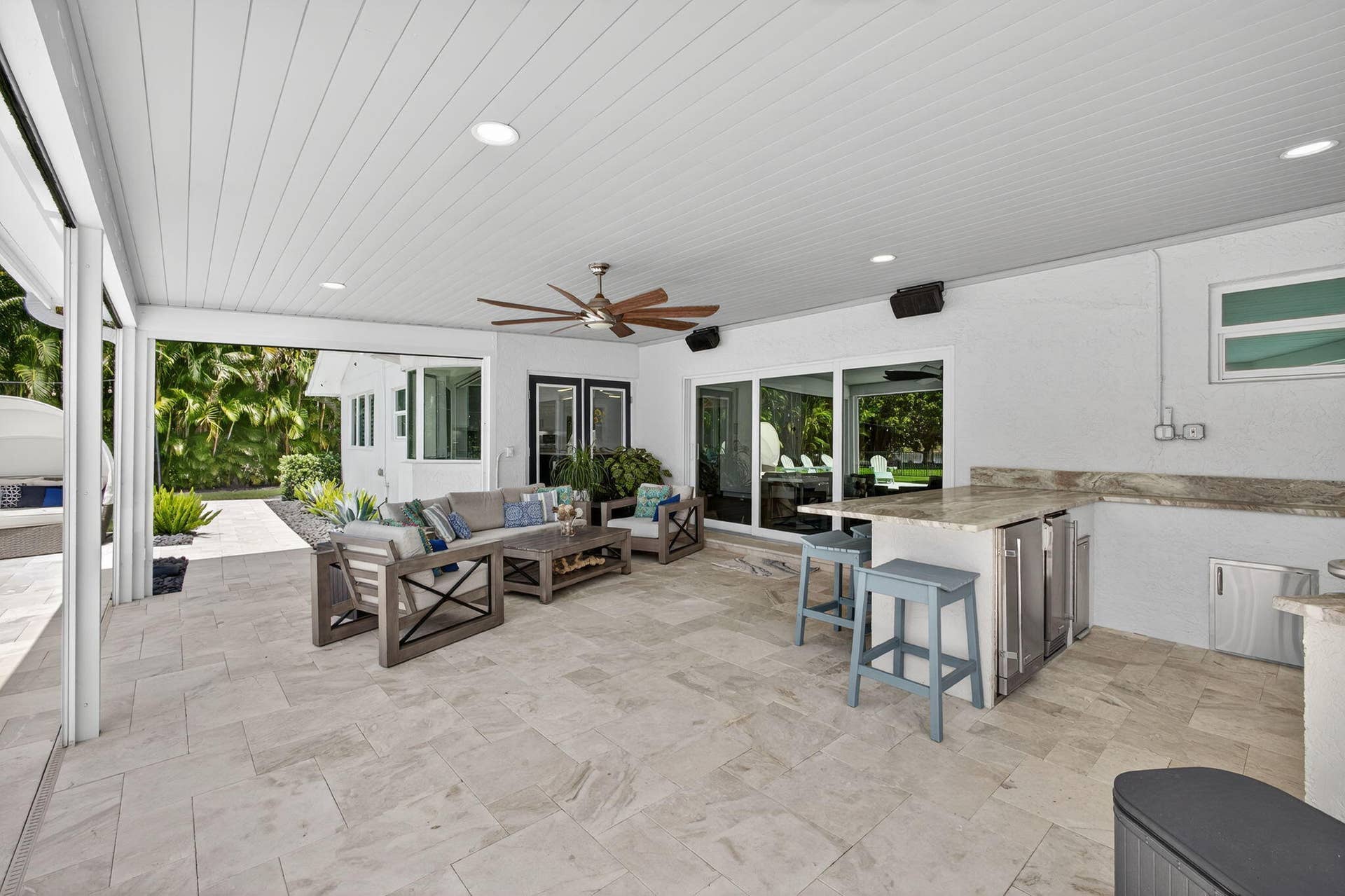 4628 Square Lake Drive, Palm Beach Gardens, FL 33418 Covered outdoor patio featuring stone tile flooring, a built-in stone-topped bar with stainless steel appliances, recessed ceiling lighting, and a mounted ceiling fan