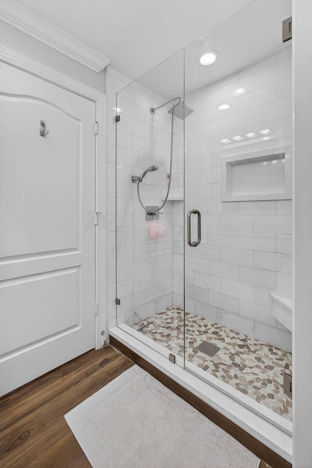 4628 Square Lake Drive, Palm Beach Gardens, FL 33418 Walk-in shower featuring a glass enclosure, subway-style wall tile, a built-in recessed niche, a pebble-stone floor, and a handheld shower fixture