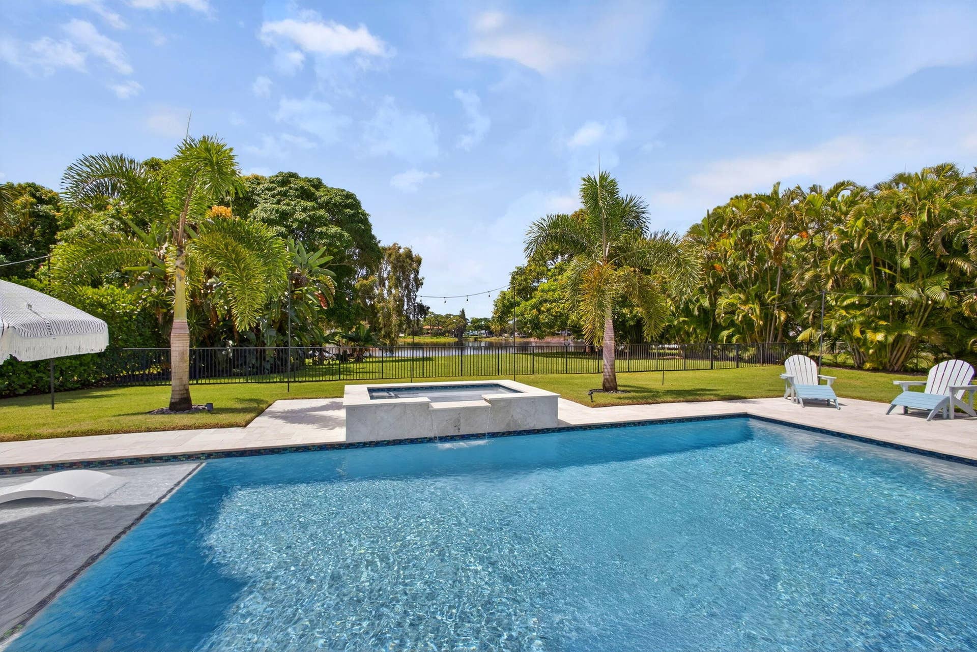 4628 Square Lake Drive, Palm Beach Gardens, FL 33418 Backyard oasis featuring a swimming pool with a stone-finish spillover spa, expansive paver patio, manicured lawn, and mature perimeter landscaping