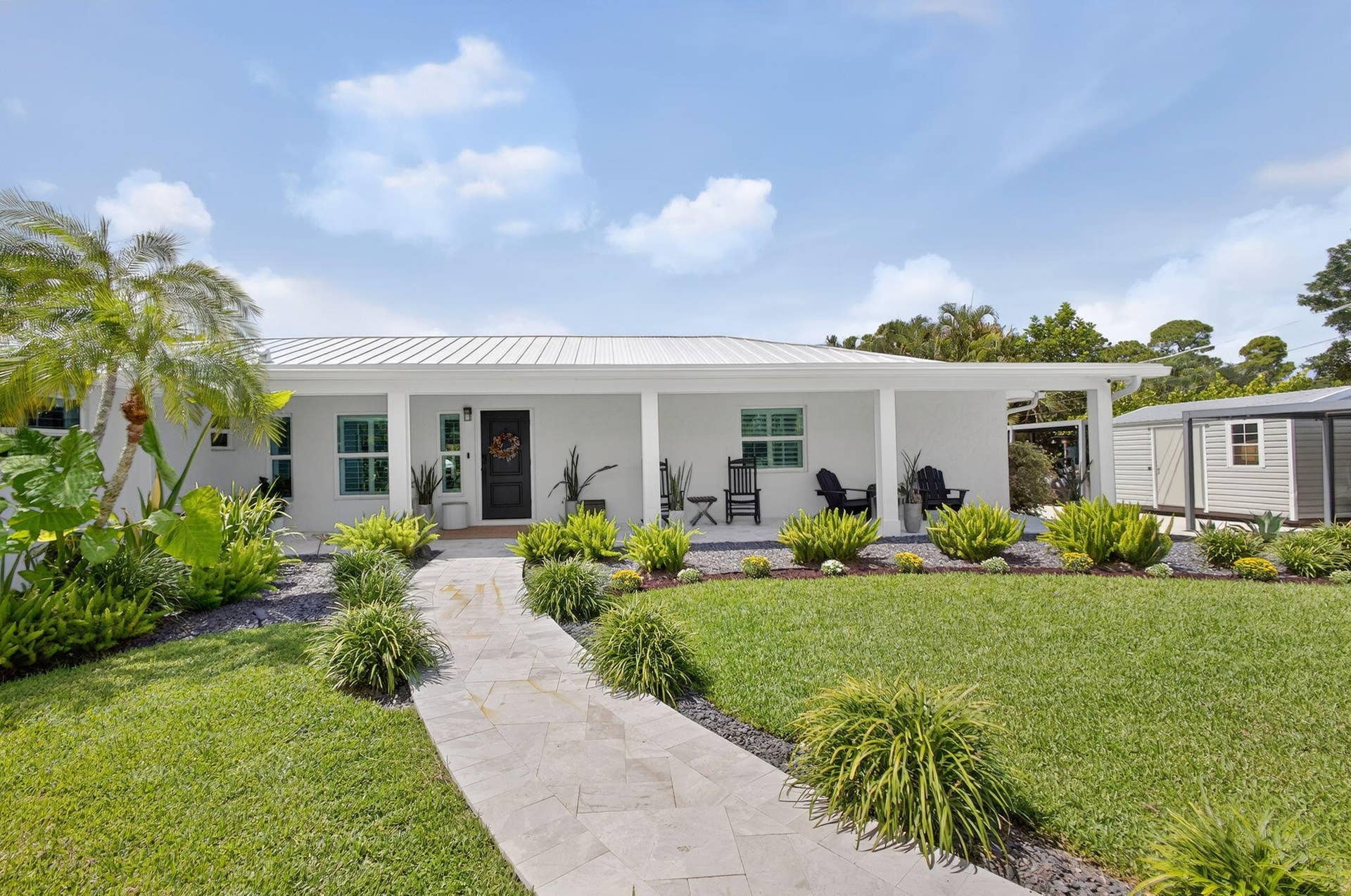 4628 Square Lake Drive, Palm Beach Gardens, FL 33418 Single-story residence featuring a metal roof, expansive front porch, stone paver walkway, and manicured landscaping