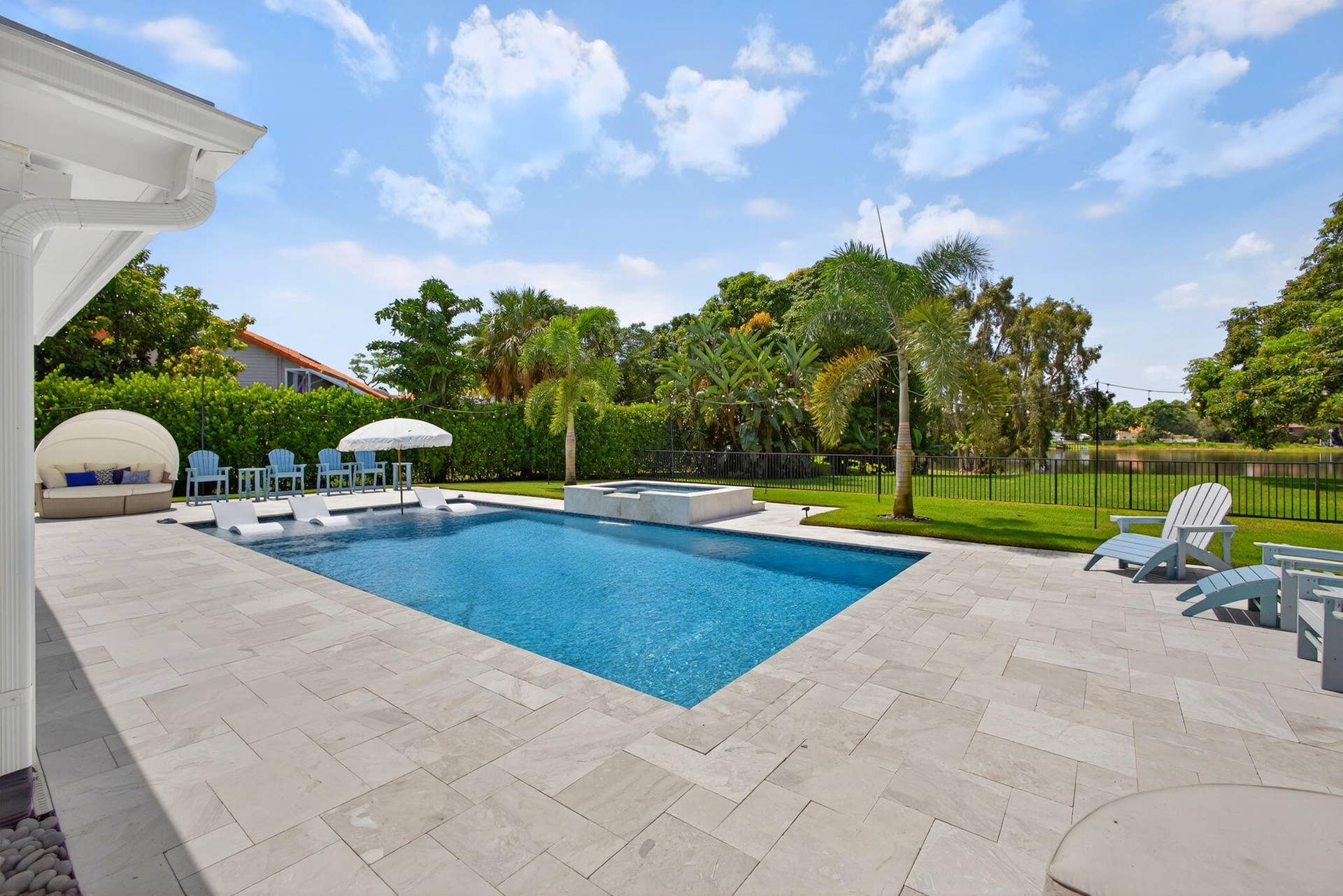 4628 Square Lake Drive, Palm Beach Gardens, FL 33418 Private backyard featuring a swimming pool with a built-in spa, expansive stone paver patio, manicured lawn, and perimeter fencing