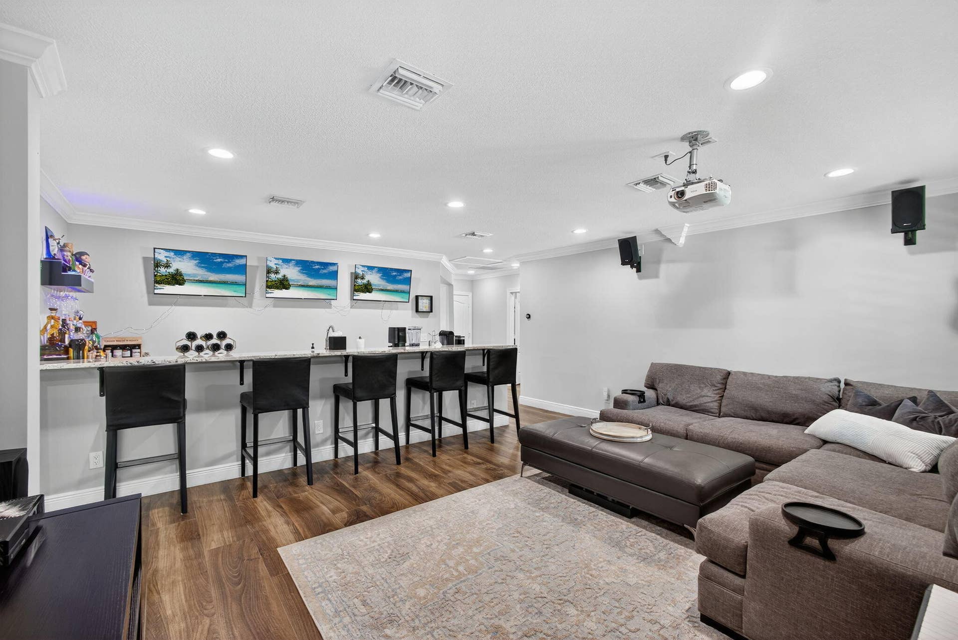 4628 Square Lake Drive, Palm Beach Gardens, FL 33418 Built-in wet bar featuring a stone-surface countertop, recessed lighting, wood-finish flooring, mounted projector, and ceiling-mounted speakers