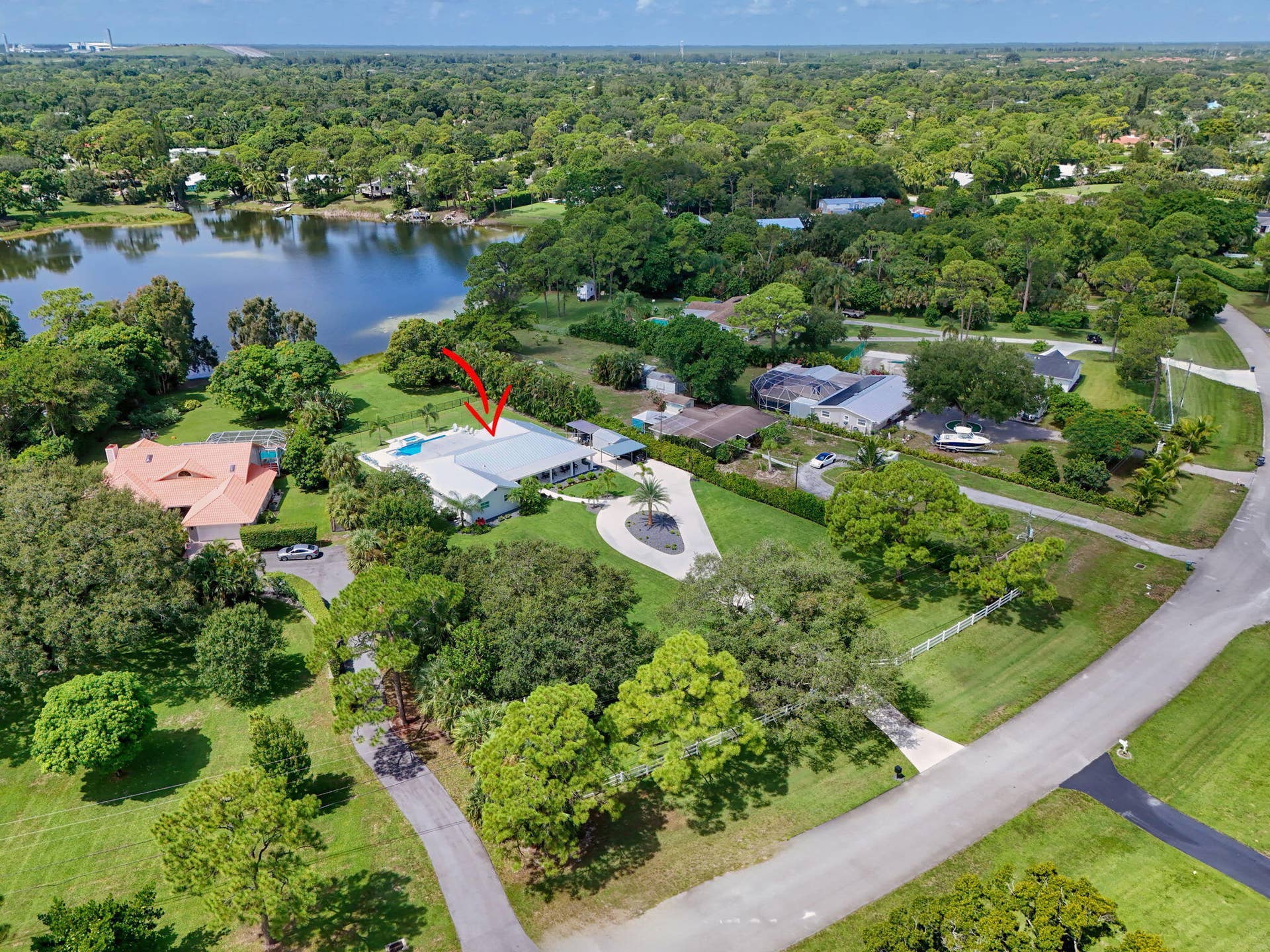 4628 Square Lake Drive, Palm Beach Gardens, FL 33418 Aerial perspective featuring a waterfront property with an in-ground swimming pool, expansive lawn, mature landscaping, and a paved circular driveway