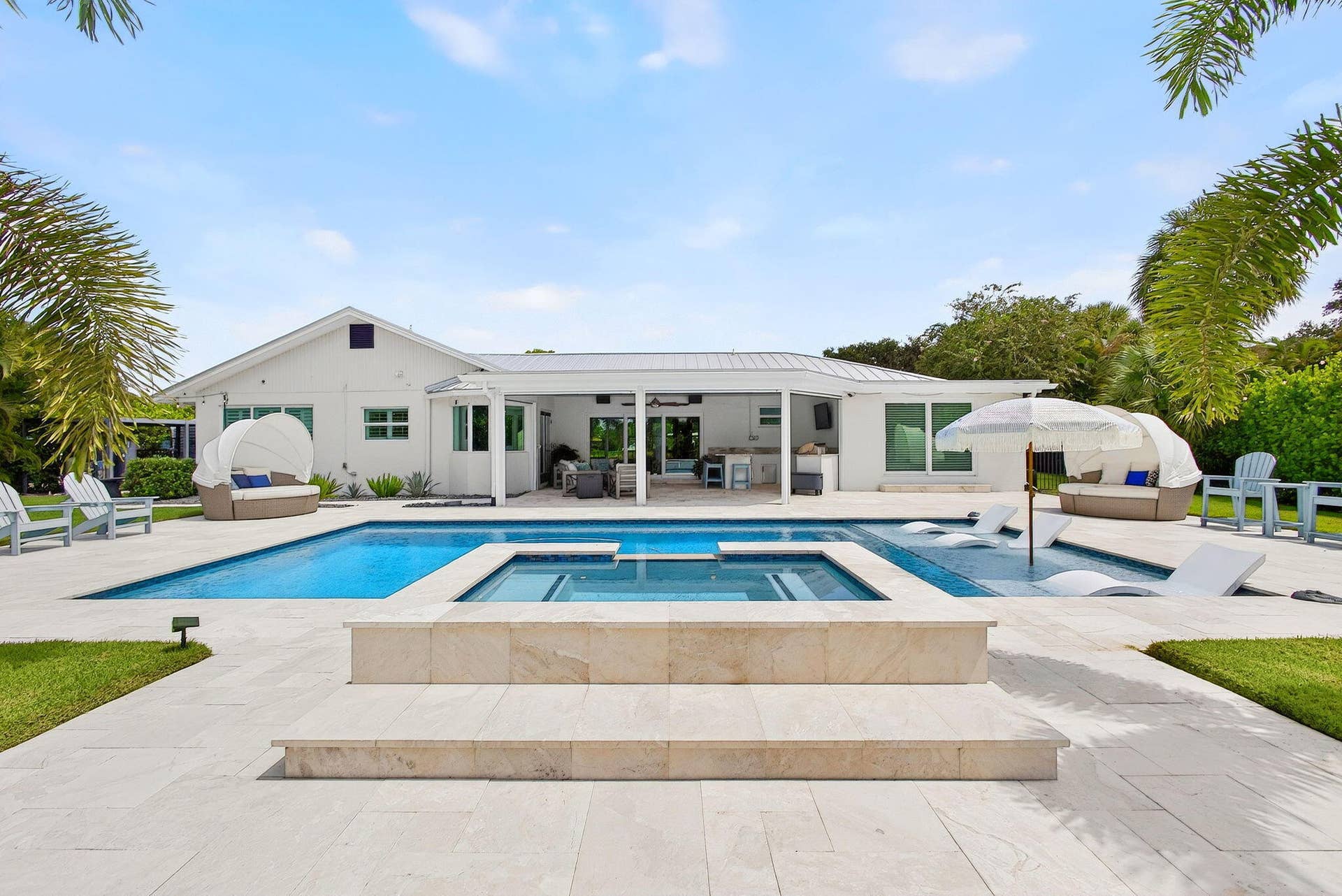 4628 Square Lake Drive, Palm Beach Gardens, FL 33418 Backyard featuring a heated in-ground pool with integrated spa, sun shelf, light-toned stone pool deck, and a covered patio