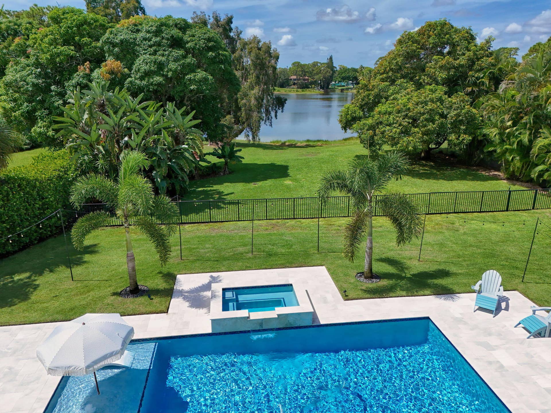 4628 Square Lake Drive, Palm Beach Gardens, FL 33418 In-ground swimming pool and attached spillover spa featuring light-colored stone decking, set against a backdrop of waterfront scenery and landscaped greenery