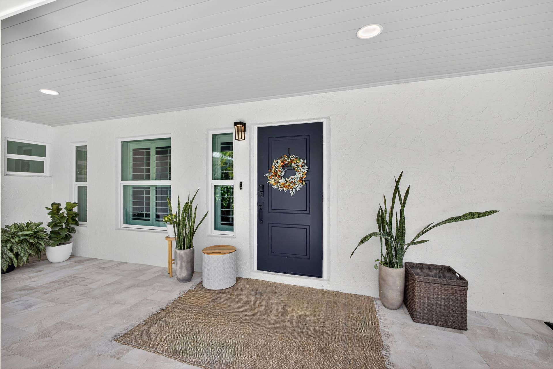 4628 Square Lake Drive, Palm Beach Gardens, FL 33418 Covered entryway featuring large-format tile flooring, a solid panel front door, recessed lighting, and white stucco exterior finish