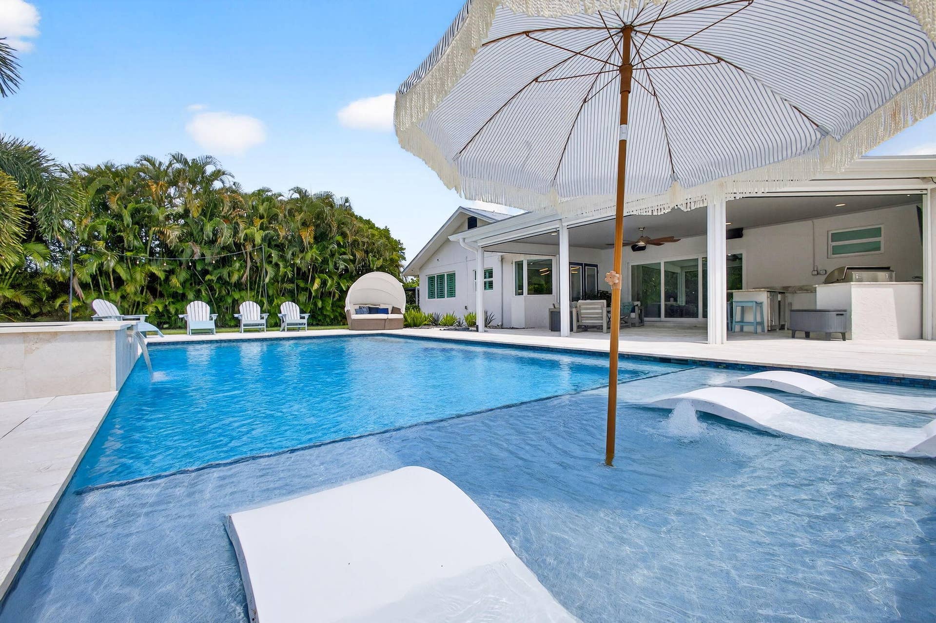 4628 Square Lake Drive, Palm Beach Gardens, FL 33418 Swimming pool featuring a sun shelf with water fountains and stone surround tiling, paired with an expansive covered outdoor living area and built-in exterior kitchen