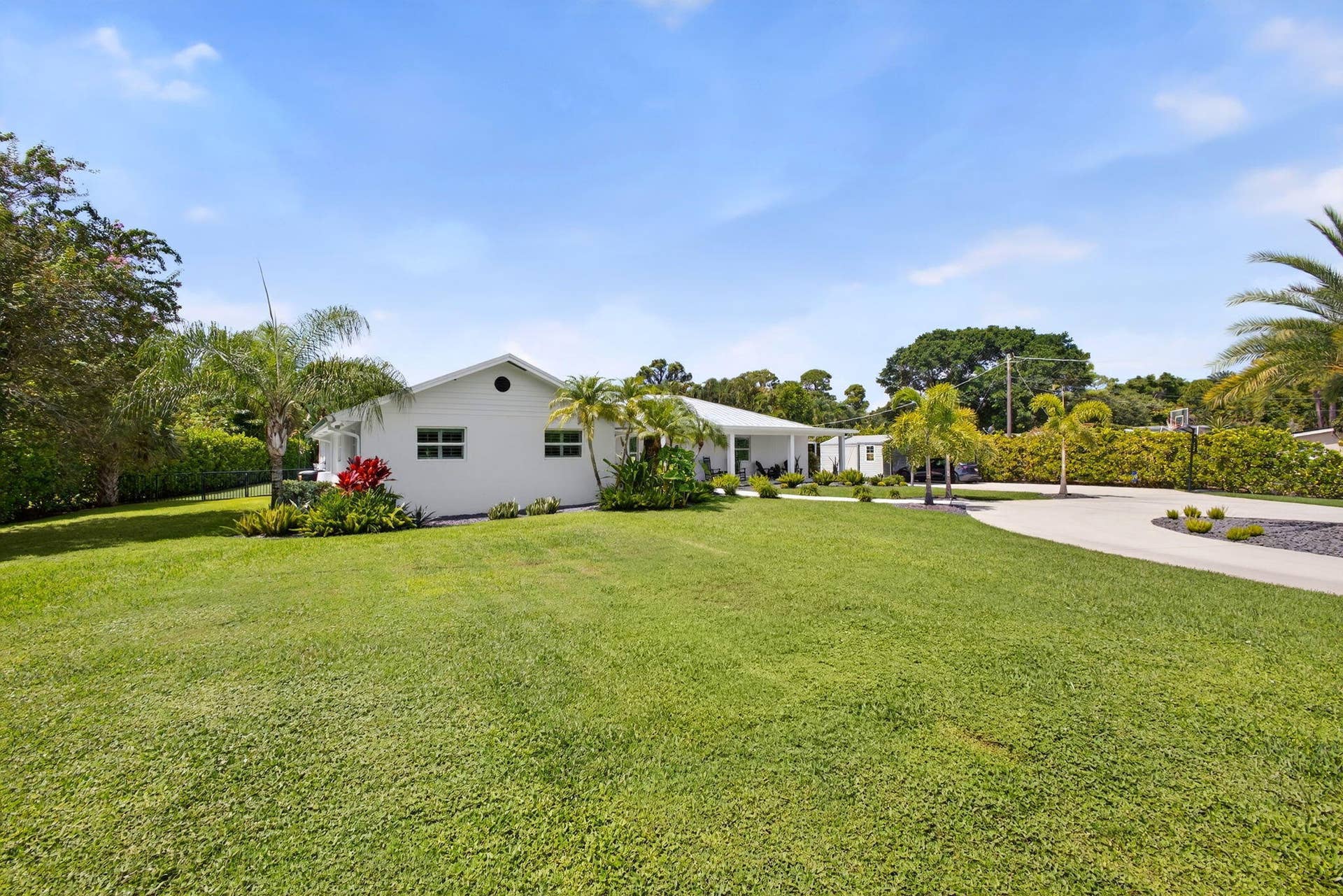 4628 Square Lake Drive, Palm Beach Gardens, FL 33418 Single-story residence featuring a painted masonry exterior, a circular concrete driveway, and expansive manicured lawn with mature palm trees