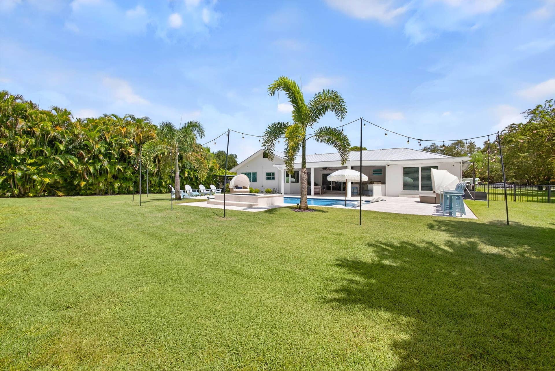 4628 Square Lake Drive, Palm Beach Gardens, FL 33418 Expansive backyard featuring a grass lawn, in-ground swimming pool, stone-paver patio, and mature perimeter landscaping