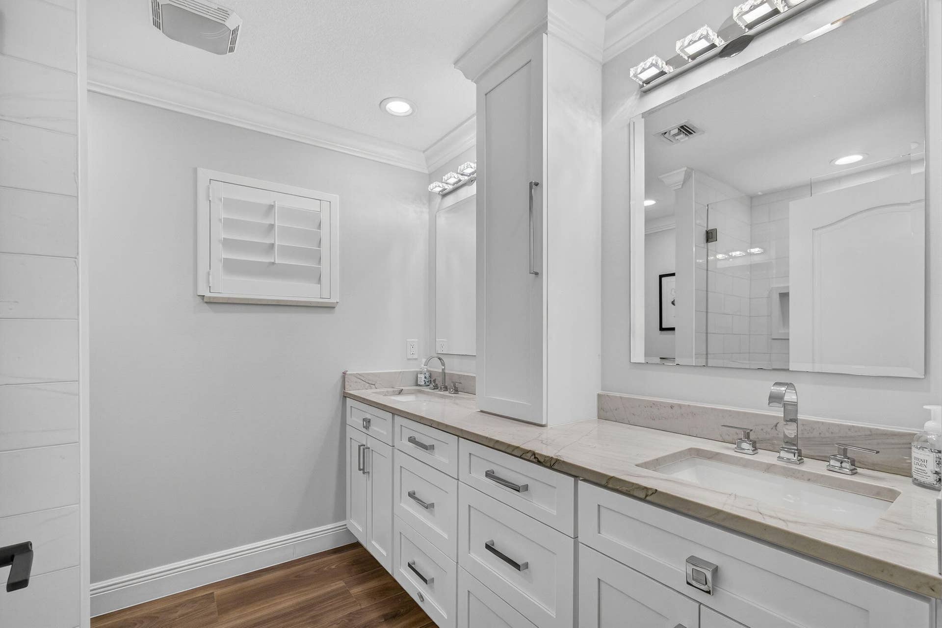 4628 Square Lake Drive, Palm Beach Gardens, FL 33418 Dual-vanity cabinetry with shaker-style white doors, stone-finish countertops, undermount rectangular sinks, chrome widespread faucets, and integrated tower storage