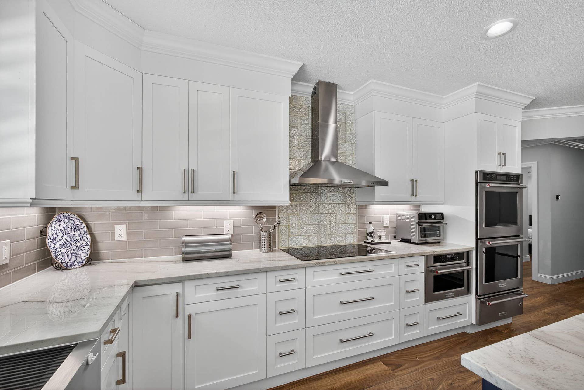 4628 Square Lake Drive, Palm Beach Gardens, FL 33418 Kitchen featuring white shaker-style cabinetry, stone-surface countertops, subway tile backsplash, stainless steel built-in double wall ovens, and wood-finish flooring