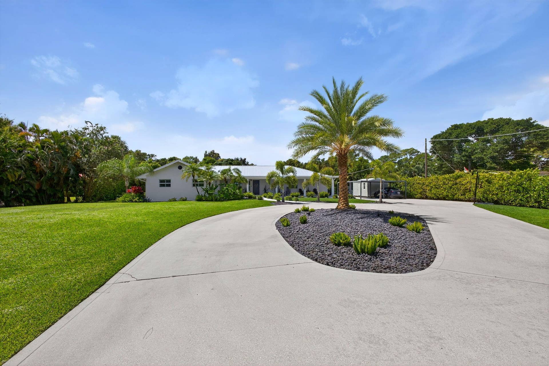 4628 Square Lake Drive, Palm Beach Gardens, FL 33418 Circular concrete driveway featuring a central landscape island with decorative stone mulch, a mature palm tree, and a manicured lawn