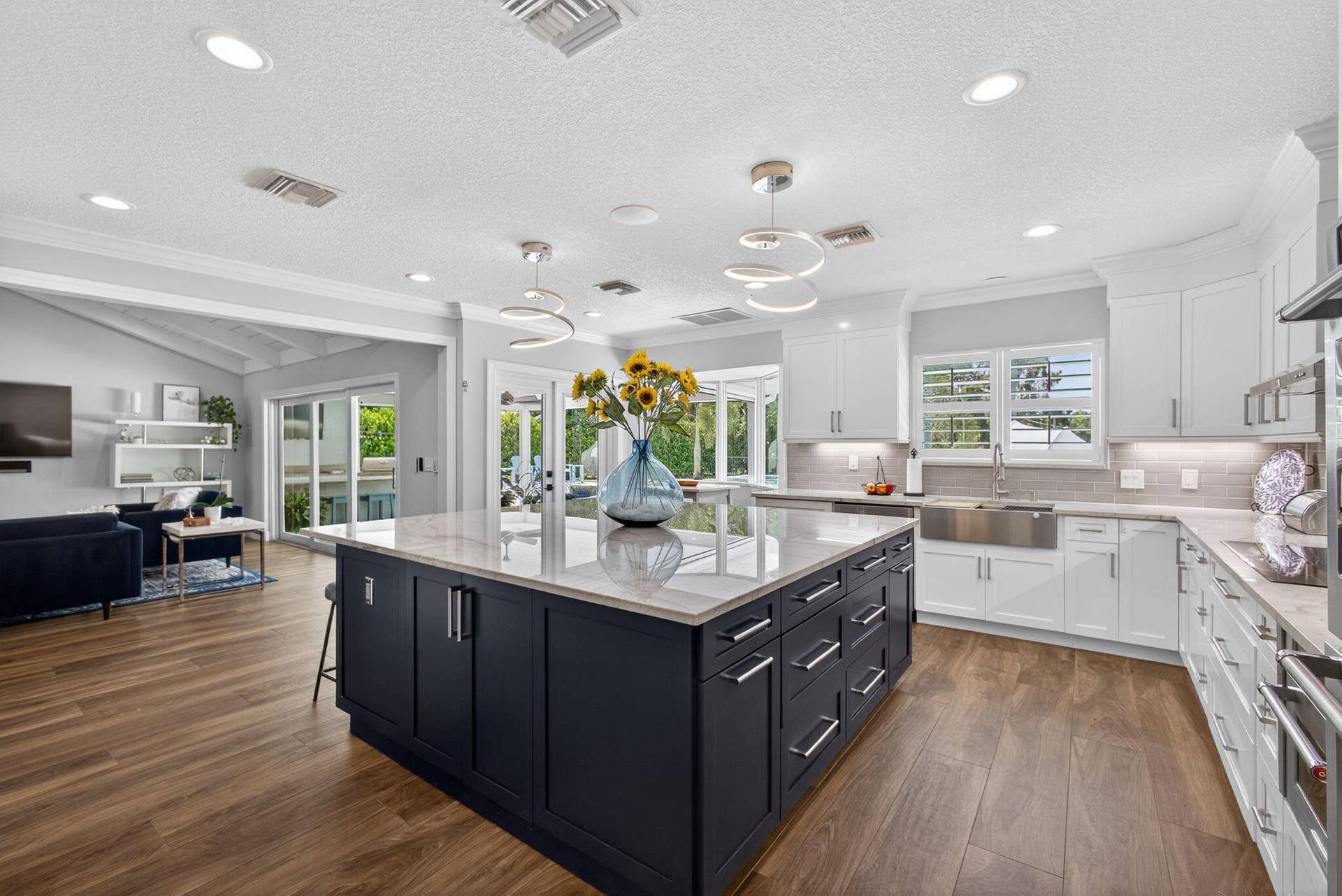 4628 Square Lake Drive, Palm Beach Gardens, FL 33418 Kitchen featuring a contrasting oversized central island, white shaker-style cabinetry, stainless steel farmhouse sink, quartz countertops, and wood-finish flooring