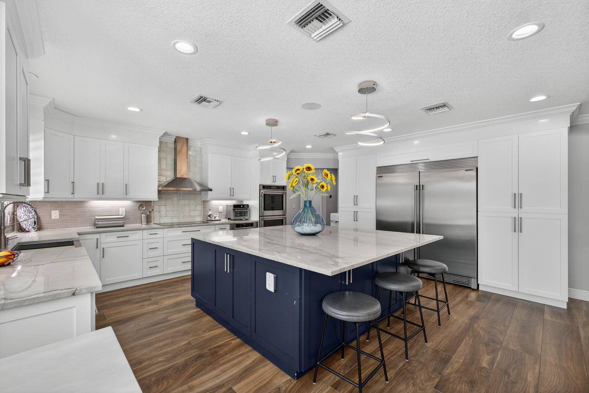 4628 Square Lake Drive, Palm Beach Gardens, FL 33418 Kitchen featuring white cabinetry, a contrasting navy blue central island with stone countertop, wood-finish flooring, stainless steel appliances, and recessed lighting