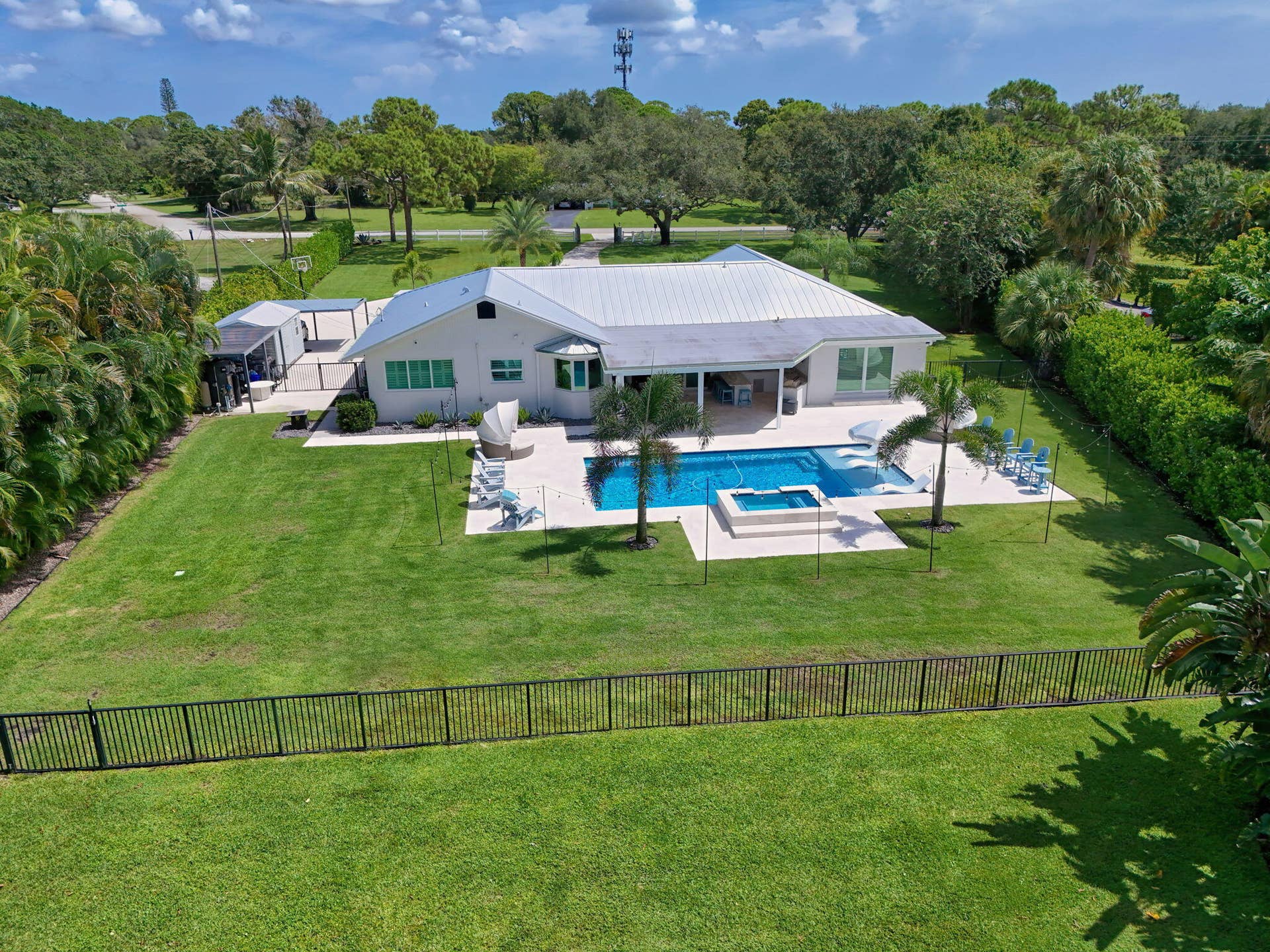 4628 Square Lake Drive, Palm Beach Gardens, FL 33418 Single-story exterior featuring a metal roof, an in-ground swimming pool with an integrated spa, a paved pool deck, and a fenced backyard