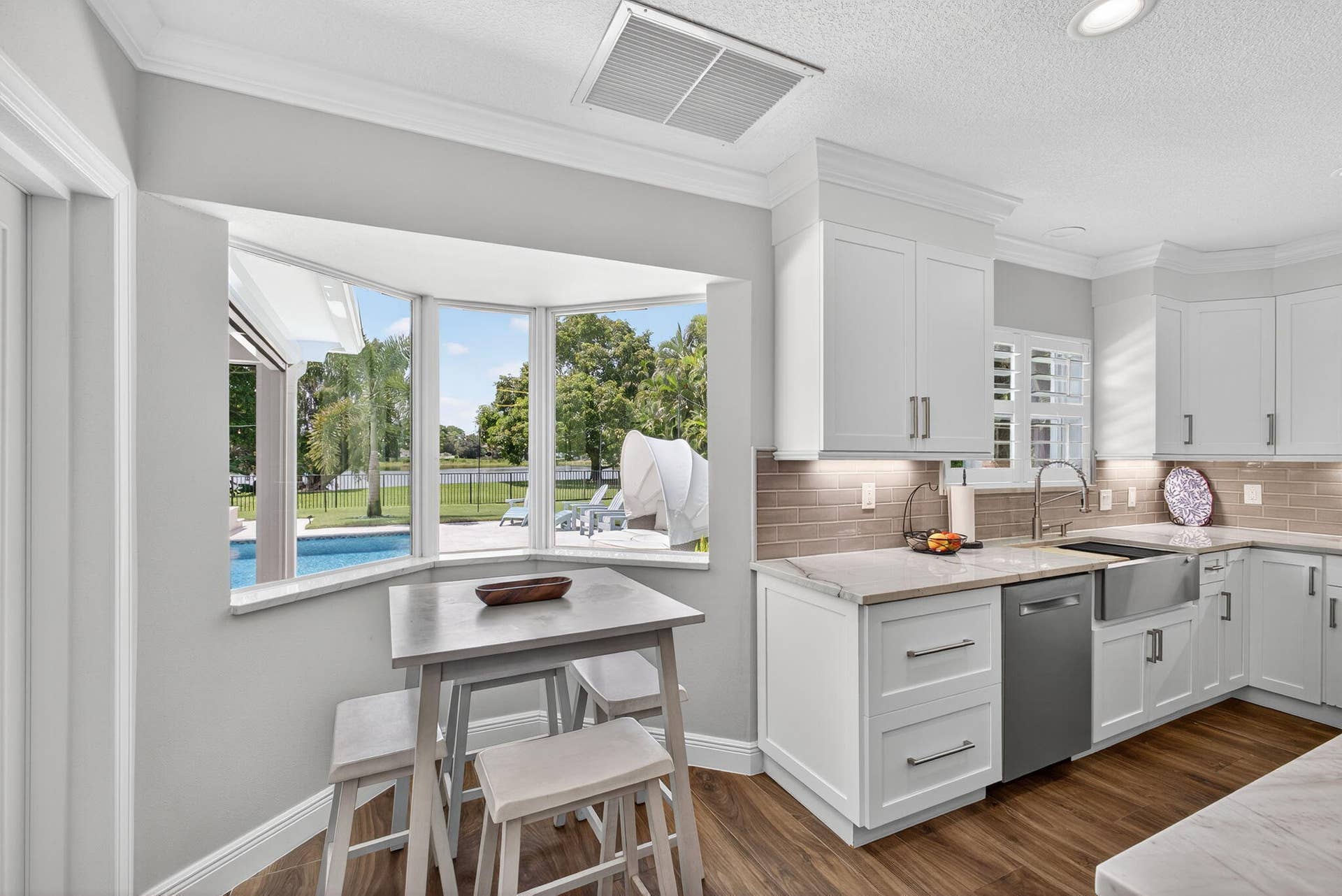 4628 Square Lake Drive, Palm Beach Gardens, FL 33418 Kitchen featuring white shaker-style cabinetry, stone-surface countertops, horizontal tile backsplash, stainless steel apron-front sink, and bay window