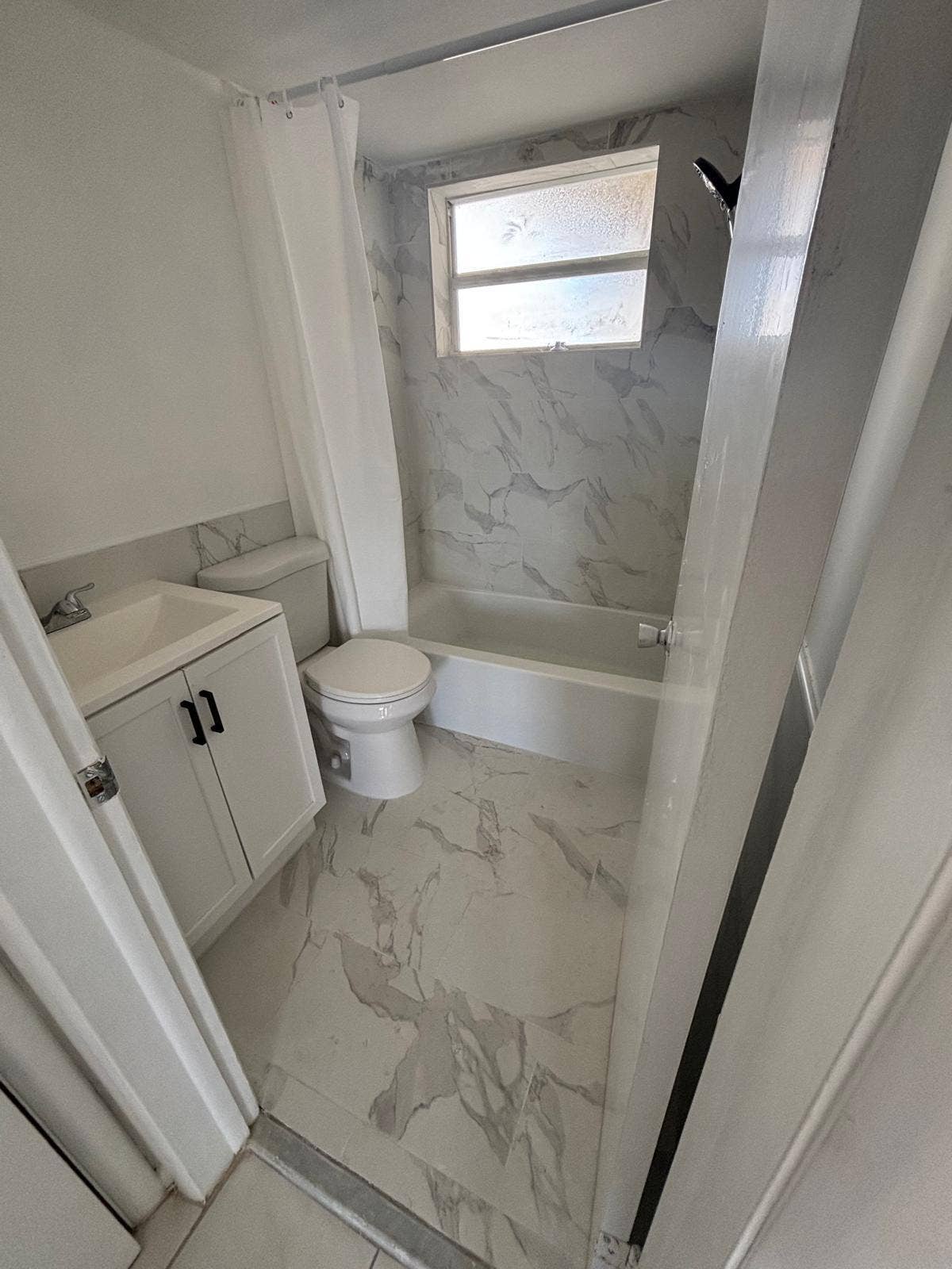 4500 S Ocean Boulevard, #310, South Palm Beach, FL 33480 Bathroom featuring stone-finish wall tile, white vanity cabinet with black hardware, integrated sink, and stone-finish floor tile