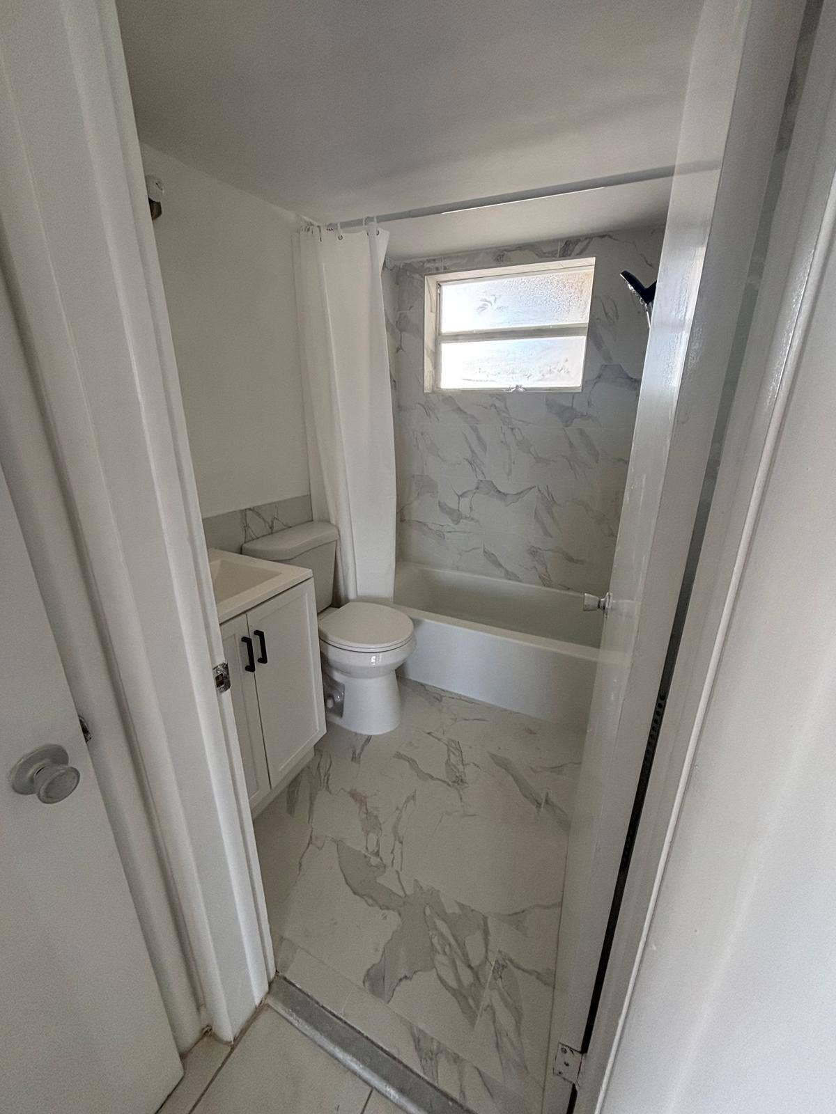 4500 S Ocean Boulevard, #310, South Palm Beach, FL 33480 Bathroom featuring stone-finish floor tiling, tub-shower combination with floor-to-ceiling stone-finish wall surrounds, single-basin vanity cabinet with matte black hardware, and an exterior window
