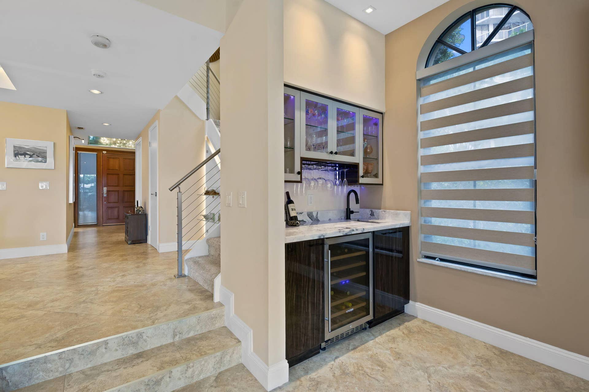 Built-in wet bar featuring dark wood-finish cabinetry, integrated wine refrigerator, stone countertop, and glass-front upper cabinets with accent lighting