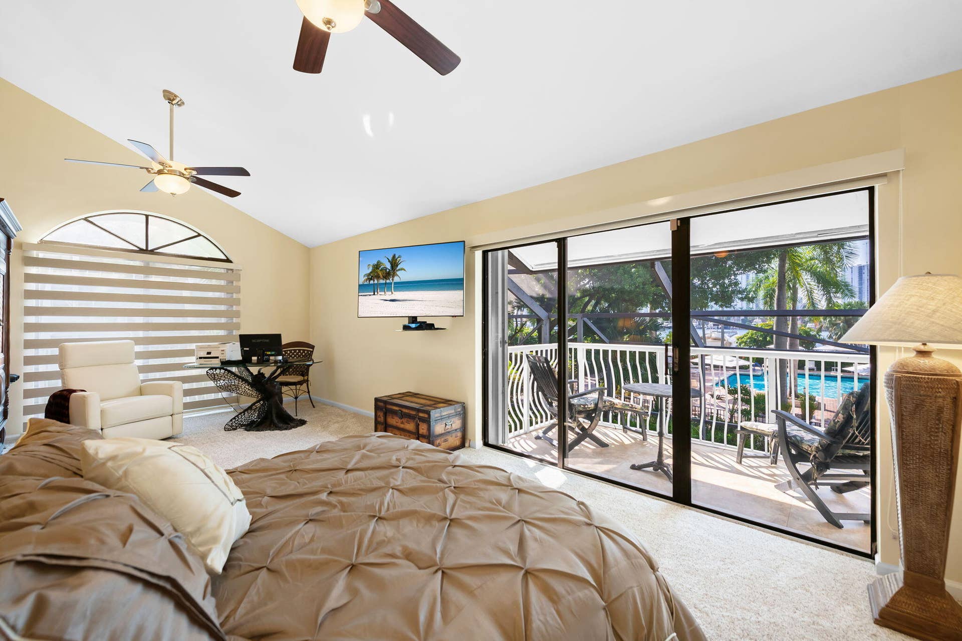 Vaulted ceilings with dual ceiling fans, expansive sliding glass doors, arched window with horizontal blinds, and a screened-in balcony