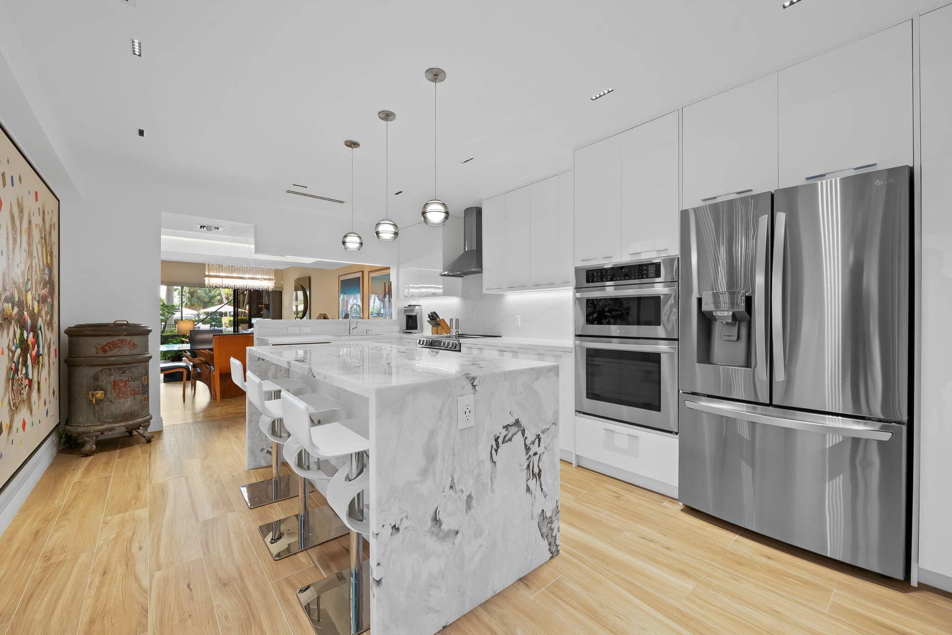 Kitchen featuring a waterfall island with stone countertop, stainless steel appliances, flat-panel cabinetry, wood-finish flooring, and recessed lighting