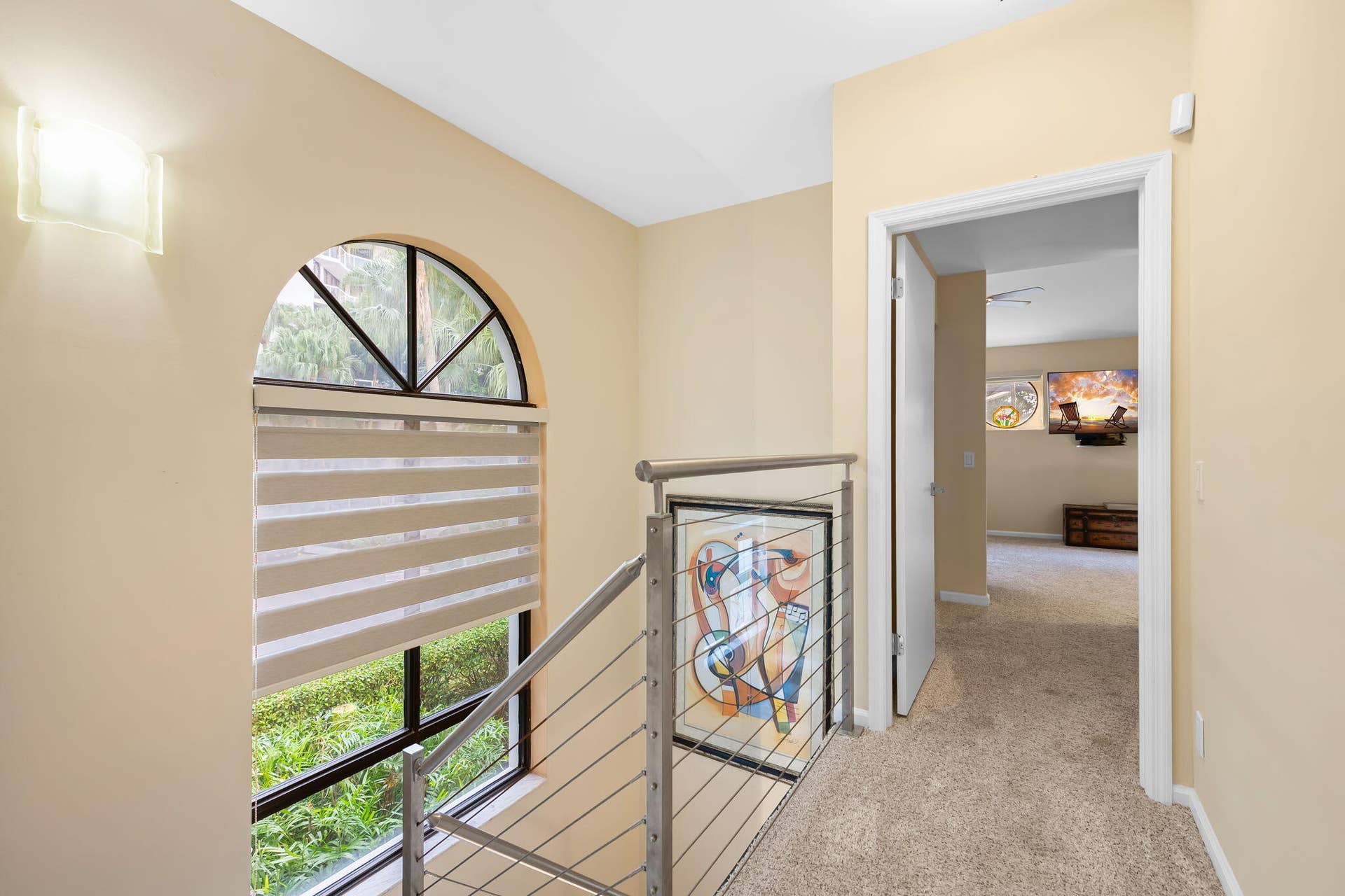 Arched window featuring a multi-pane design, complemented by a contemporary stainless steel cable railing system and wall-mounted sconce lighting