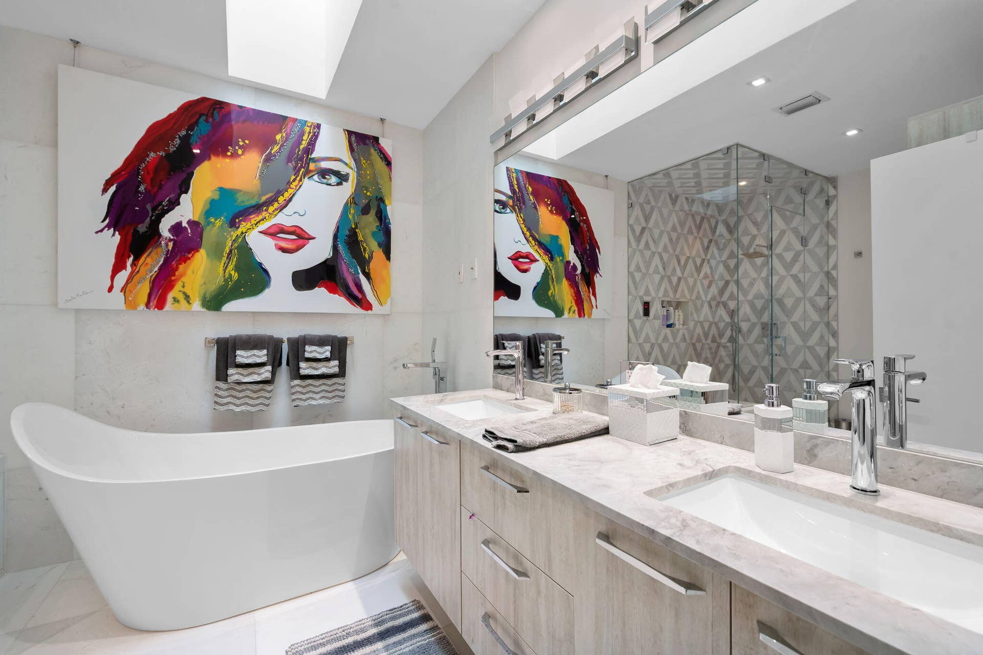 Skylight, freestanding soaking tub, double-sink vanity with stone countertop, walk-in glass-enclosed shower, and recessed ceiling lighting